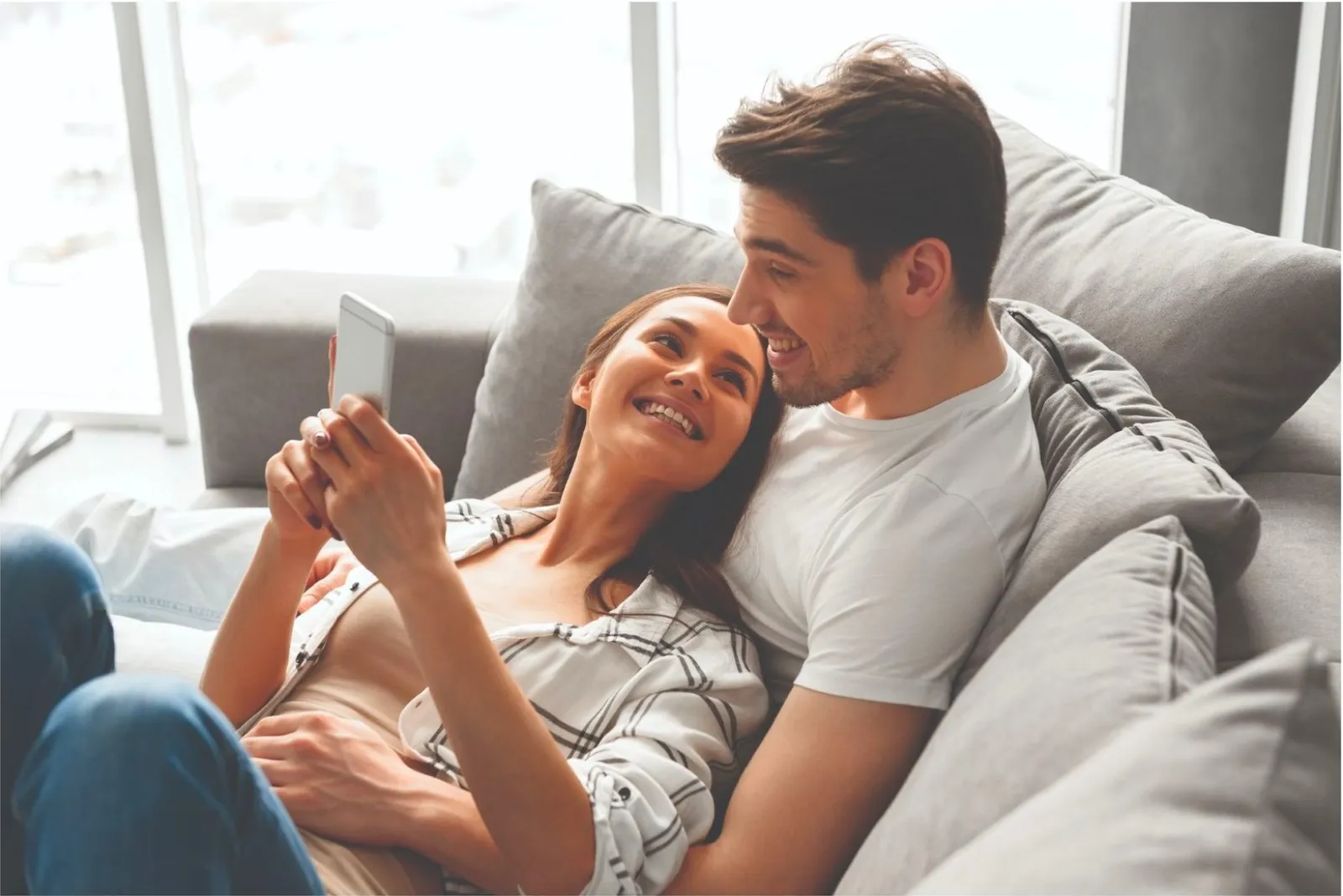 a man and a woman sitting on a couch and looking at a cell phone