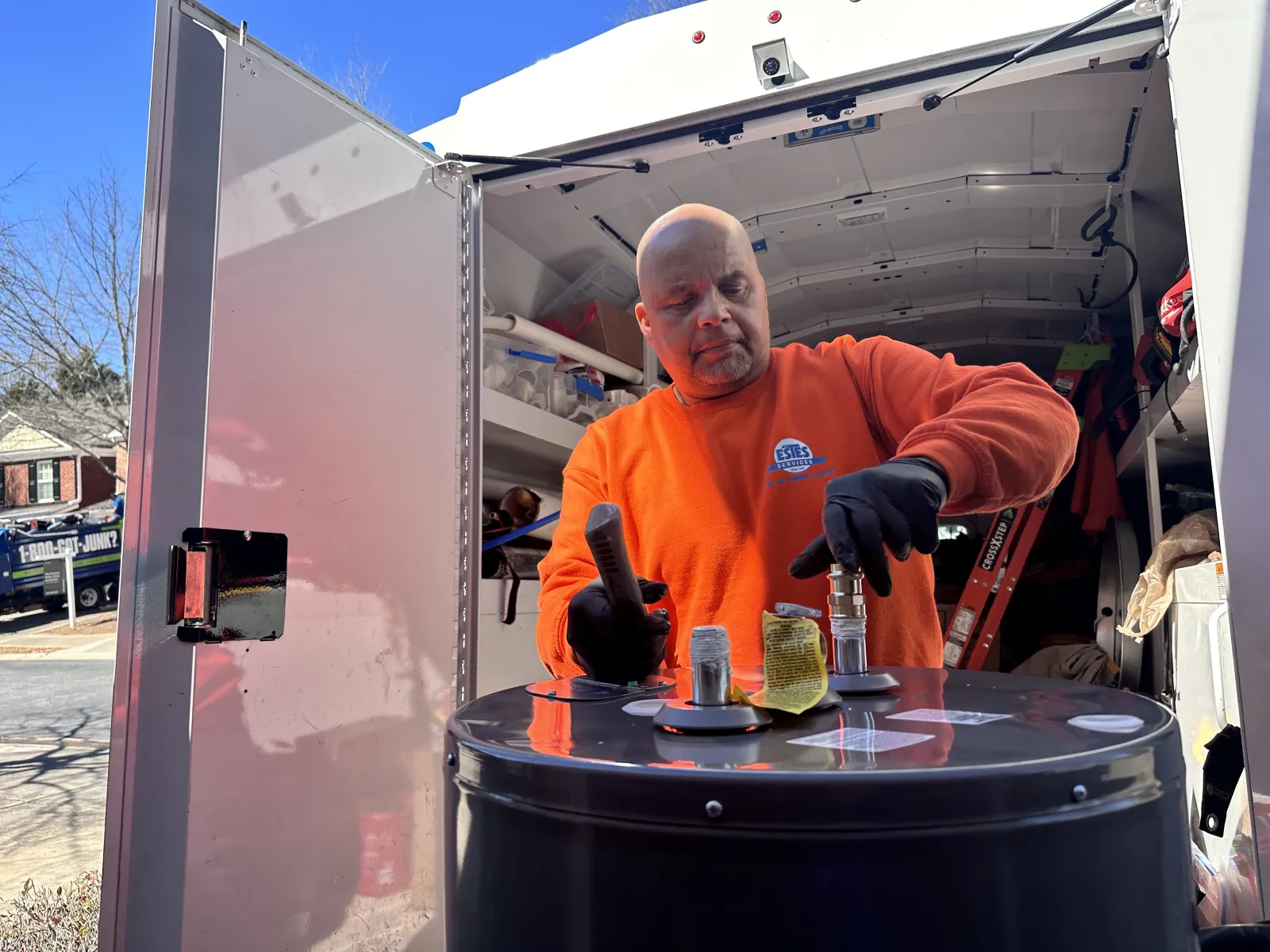 Estes Plumber in orange sweatshirt uniform replacing a tank water heater