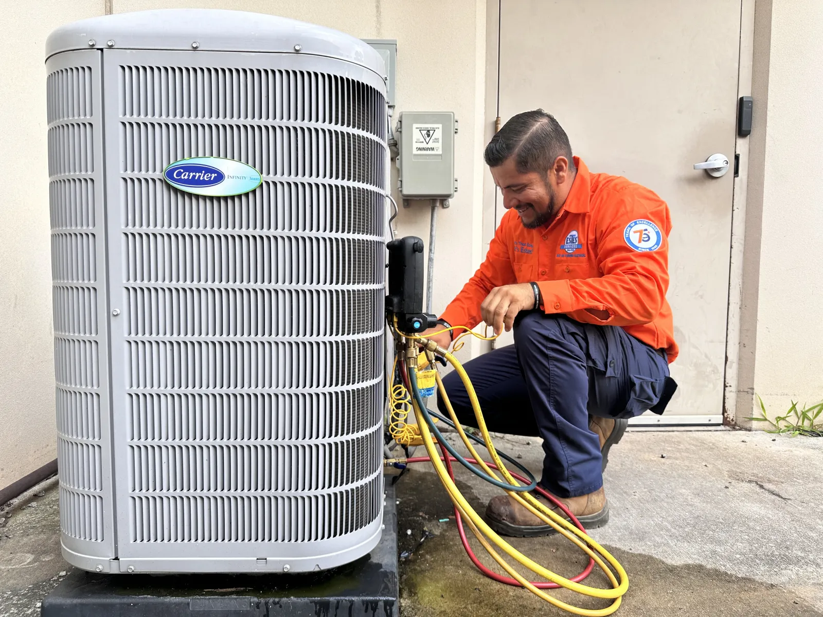 Estes Services Technician in orange uniform installing a Heat Pump with the Georgia HEAR Programith diagnostic tools and colorful cables outdoors.