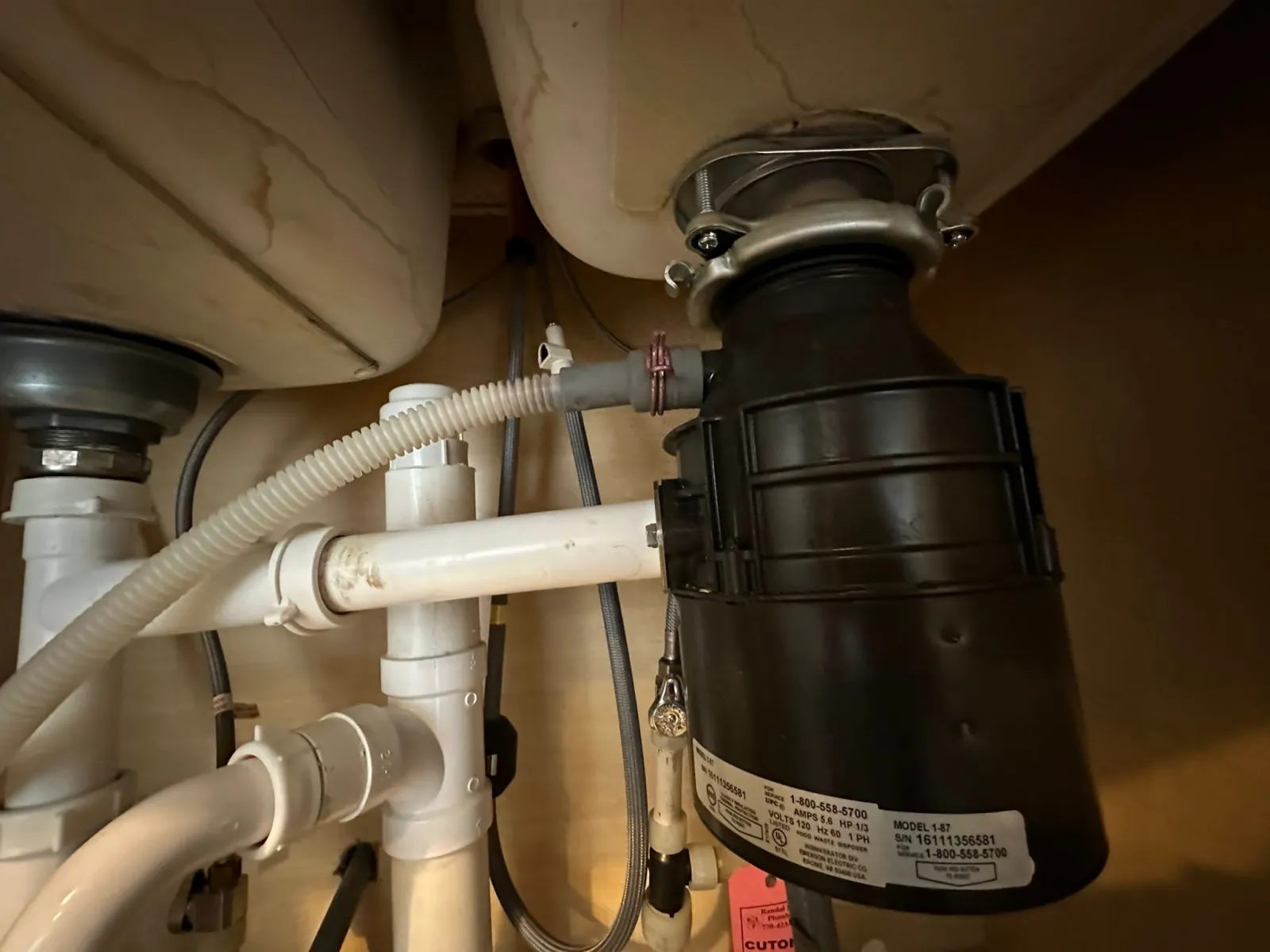 Under-sink garbage disposal unit with visible plumbing connections and mounting hardware.