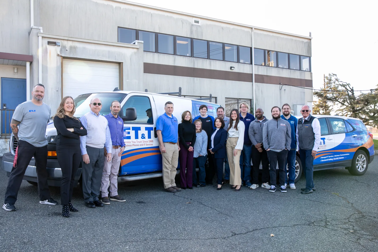 Group of diverse professionals standing in front of company-branded van and SUV outside an office building.