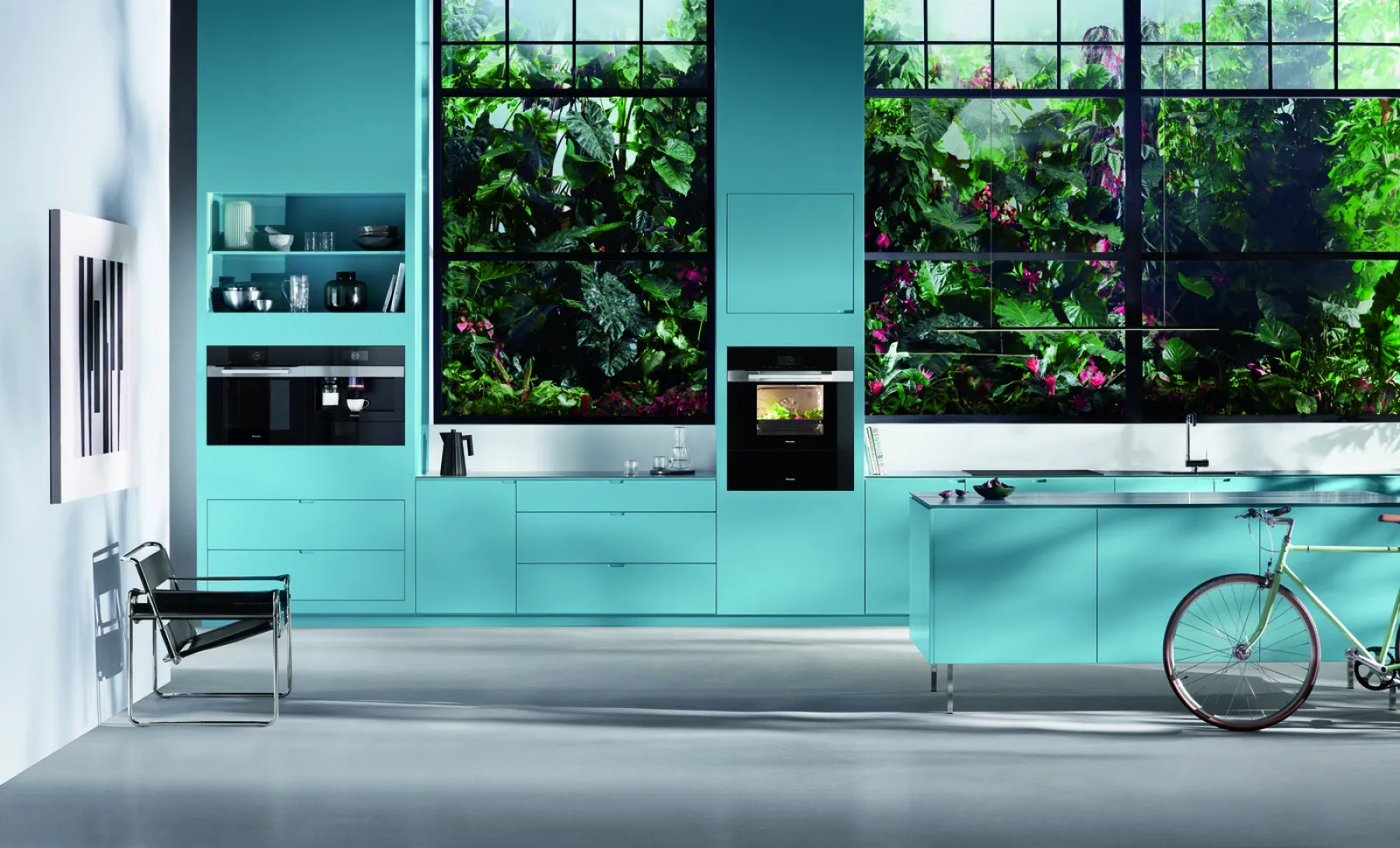 Modern turquoise kitchen with large windows showcasing lush greenery outside.