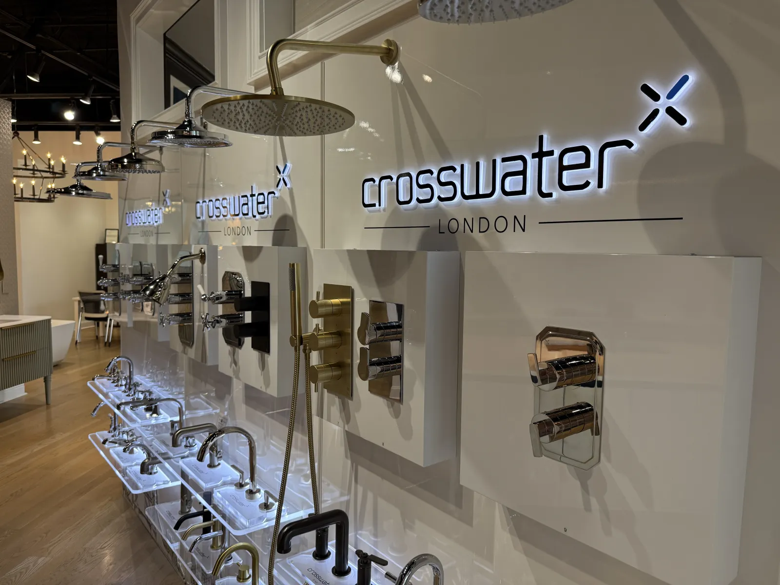 Display of luxury Crosswater London faucets and showerheads in a showroom with wood flooring and modern lighting.