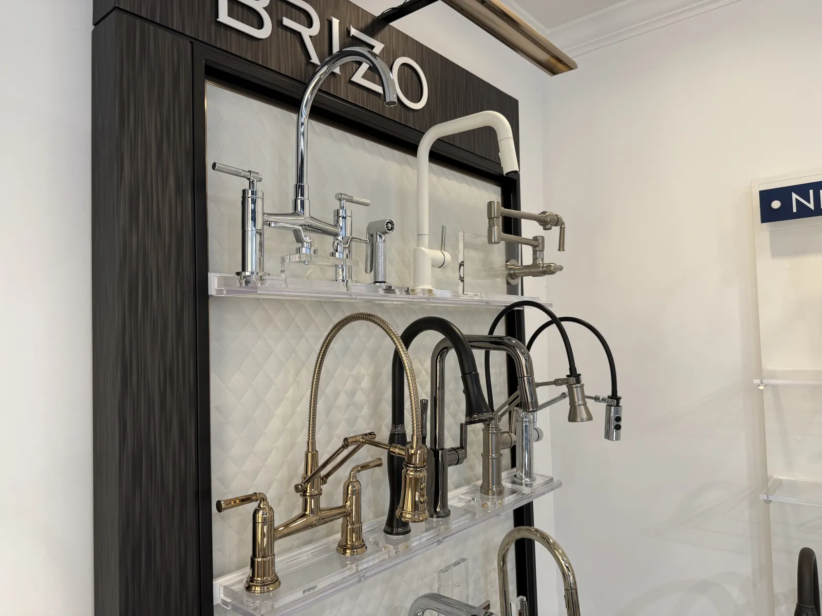 Display of Brizo brand kitchen faucets in various styles and finishes on a showroom wall mount.