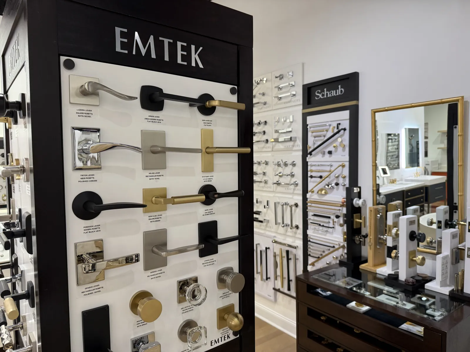 Display of various Emtek door handles and knobs in finishes like brass, black, and chrome in showroom setting.
