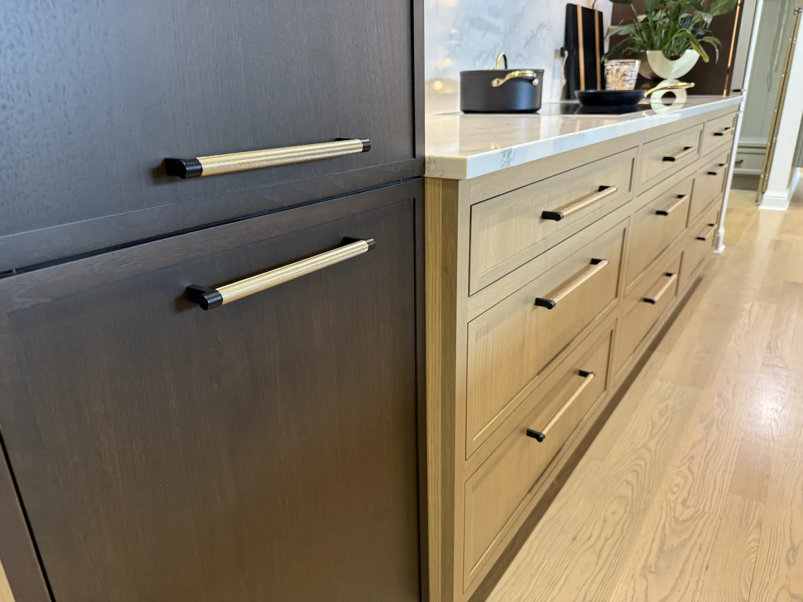 Modern kitchen cabinets with two-tone wood finish and brass handles under a white countertop on hardwood floor.