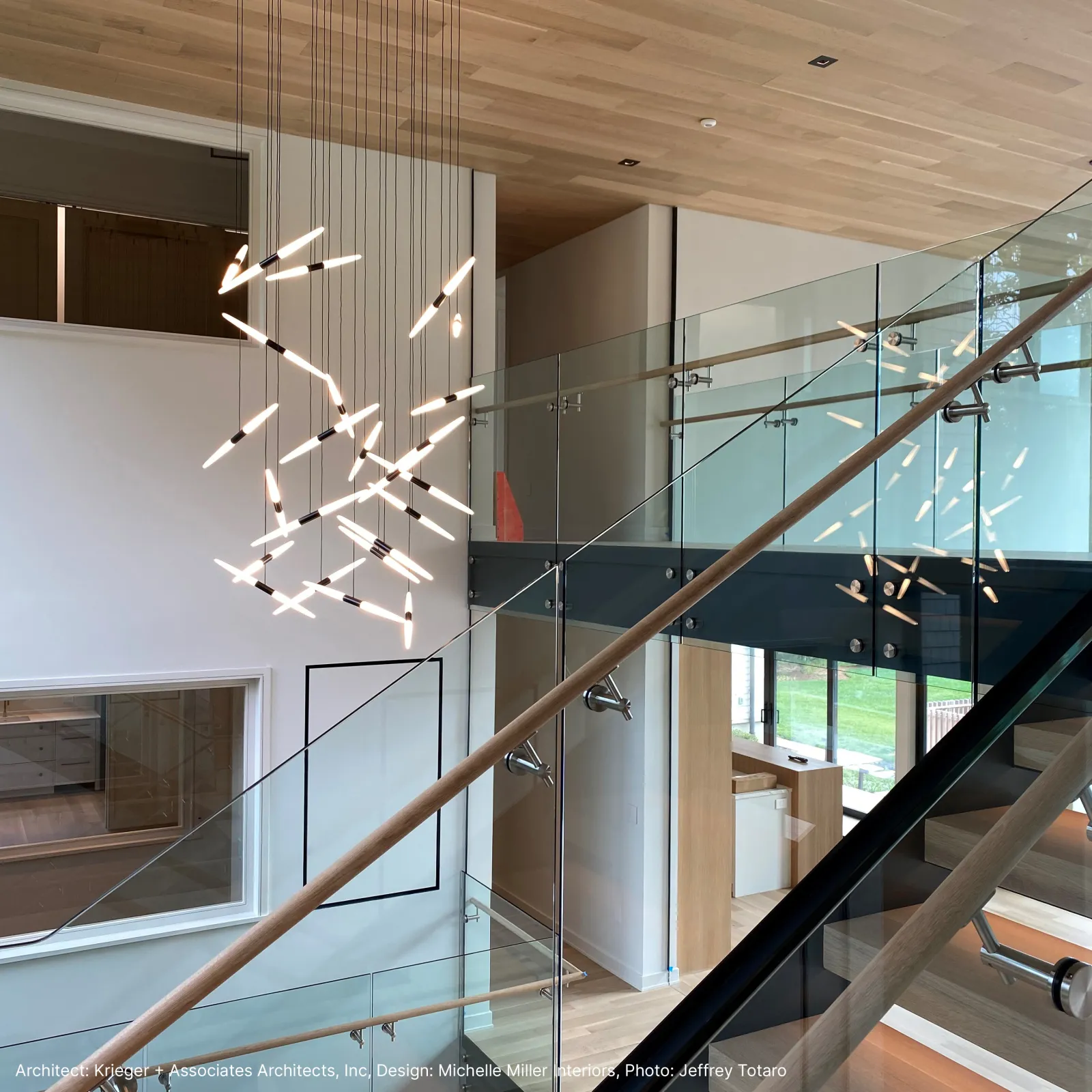 Modern staircase with glass railings and a contemporary pendant light fixture in a spacious interior.