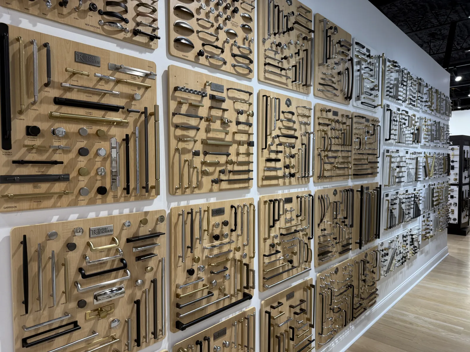 Wall display of various metal cabinet handles and knobs in different styles and finishes at a hardware store.