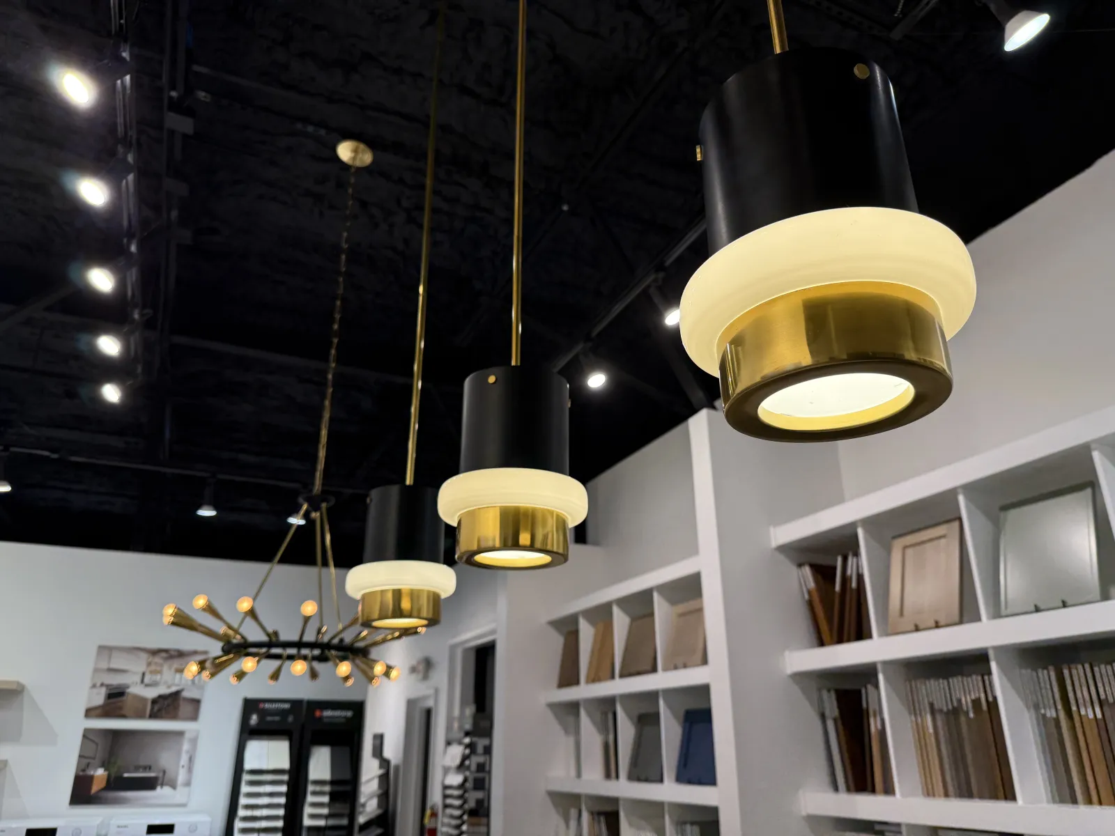 Modern pendant lights with gold and black design hanging from ceiling in a showroom with samples on shelves.
