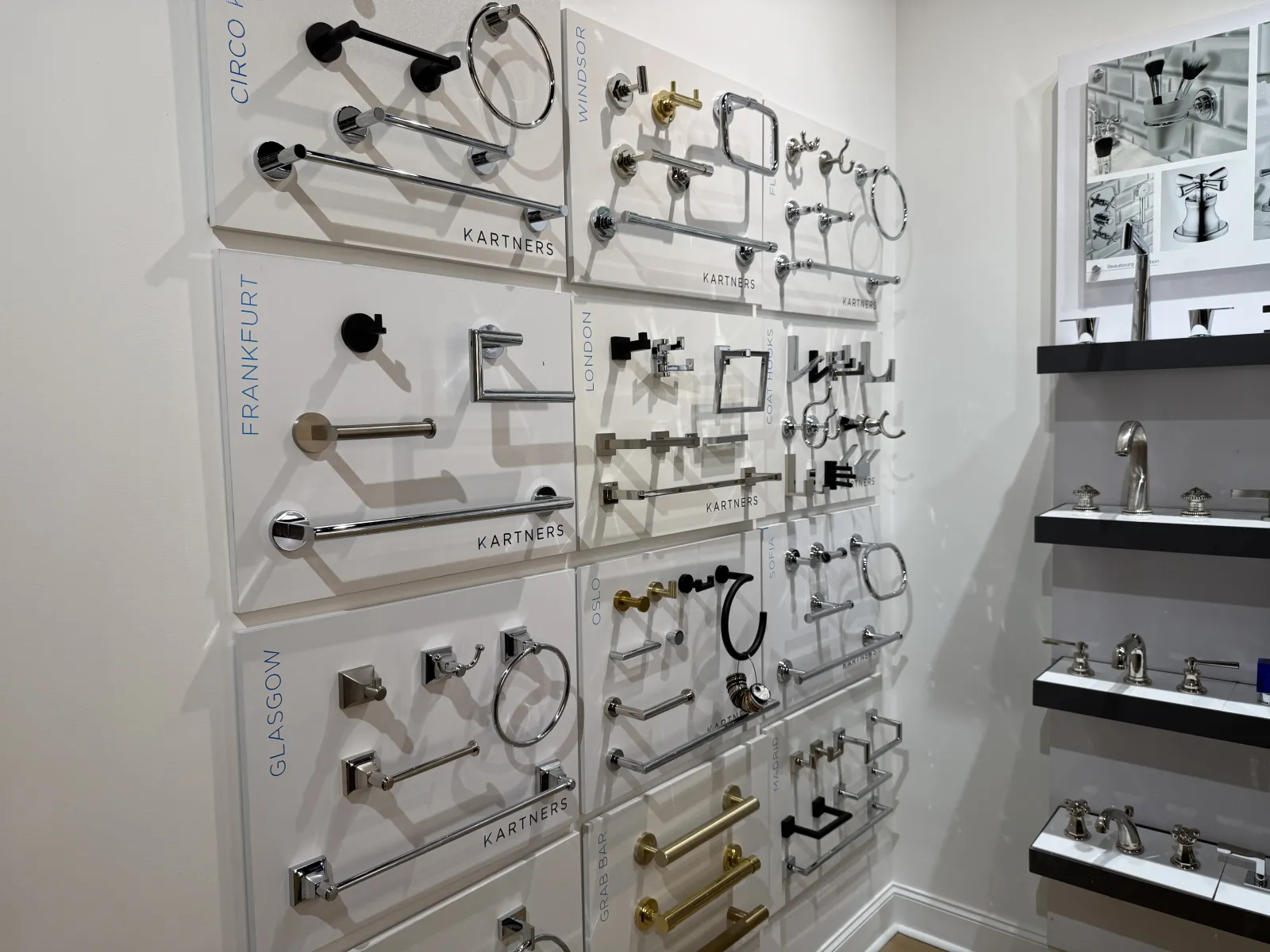 Wall display of various modern bathroom hardware including towel racks, rings, and hooks in metal finishes.