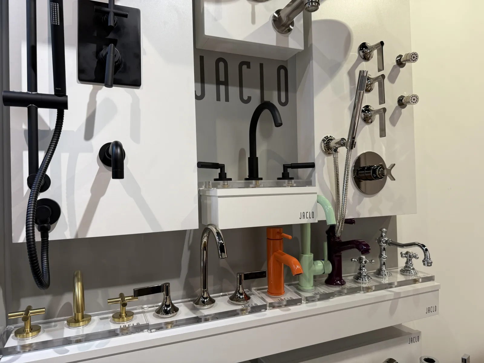 Display of diverse modern faucets and shower fixtures in various finishes and colors at a showroom.