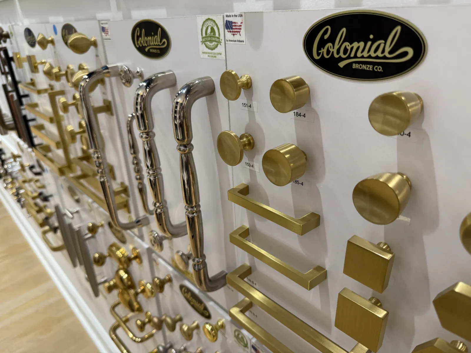 Display of various gold and silver door handles, knobs, and pulls mounted on white boards.