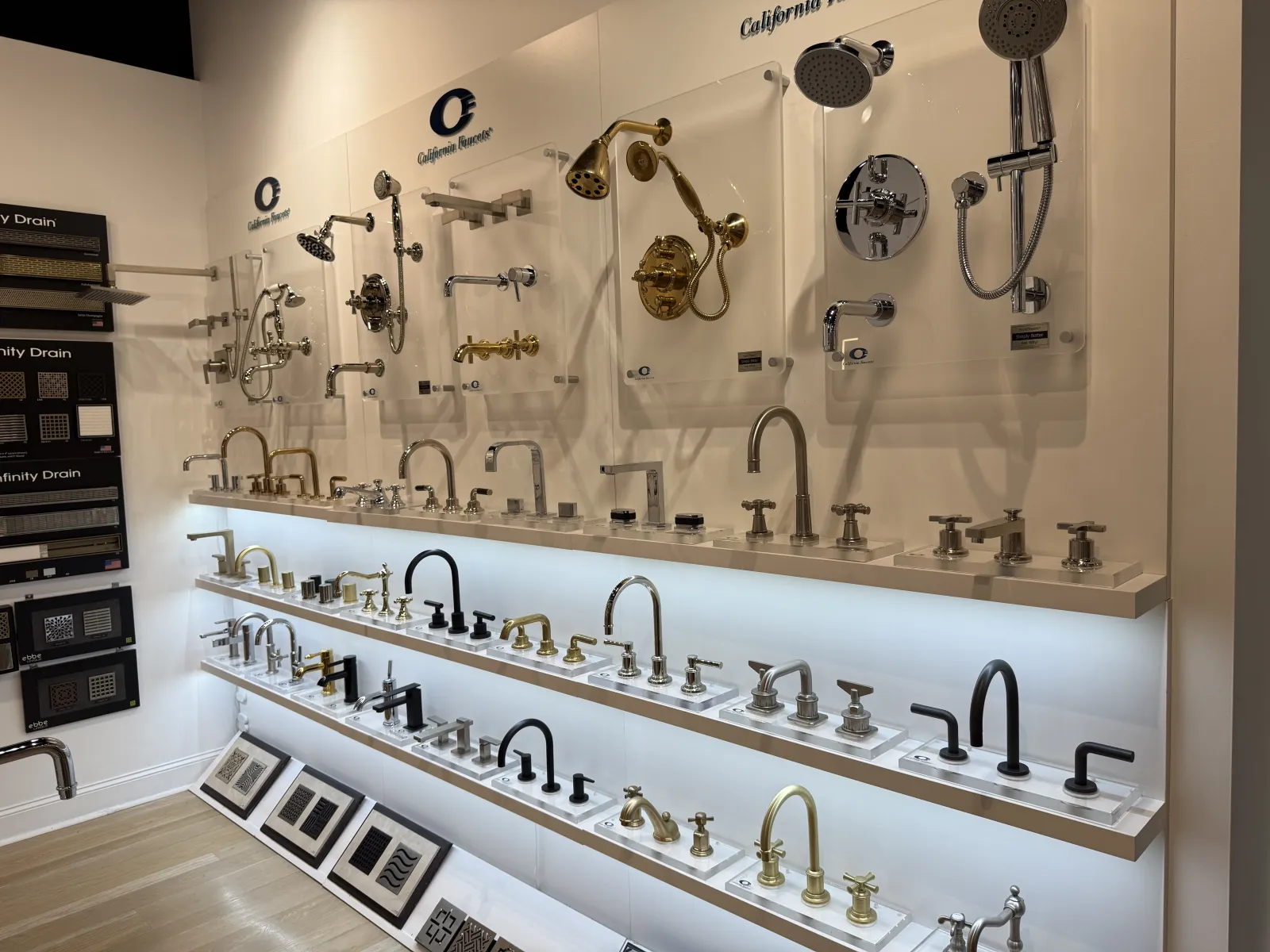 Display of various modern bathroom faucets and showerheads in silver, gold, and black finishes on backlit shelves.