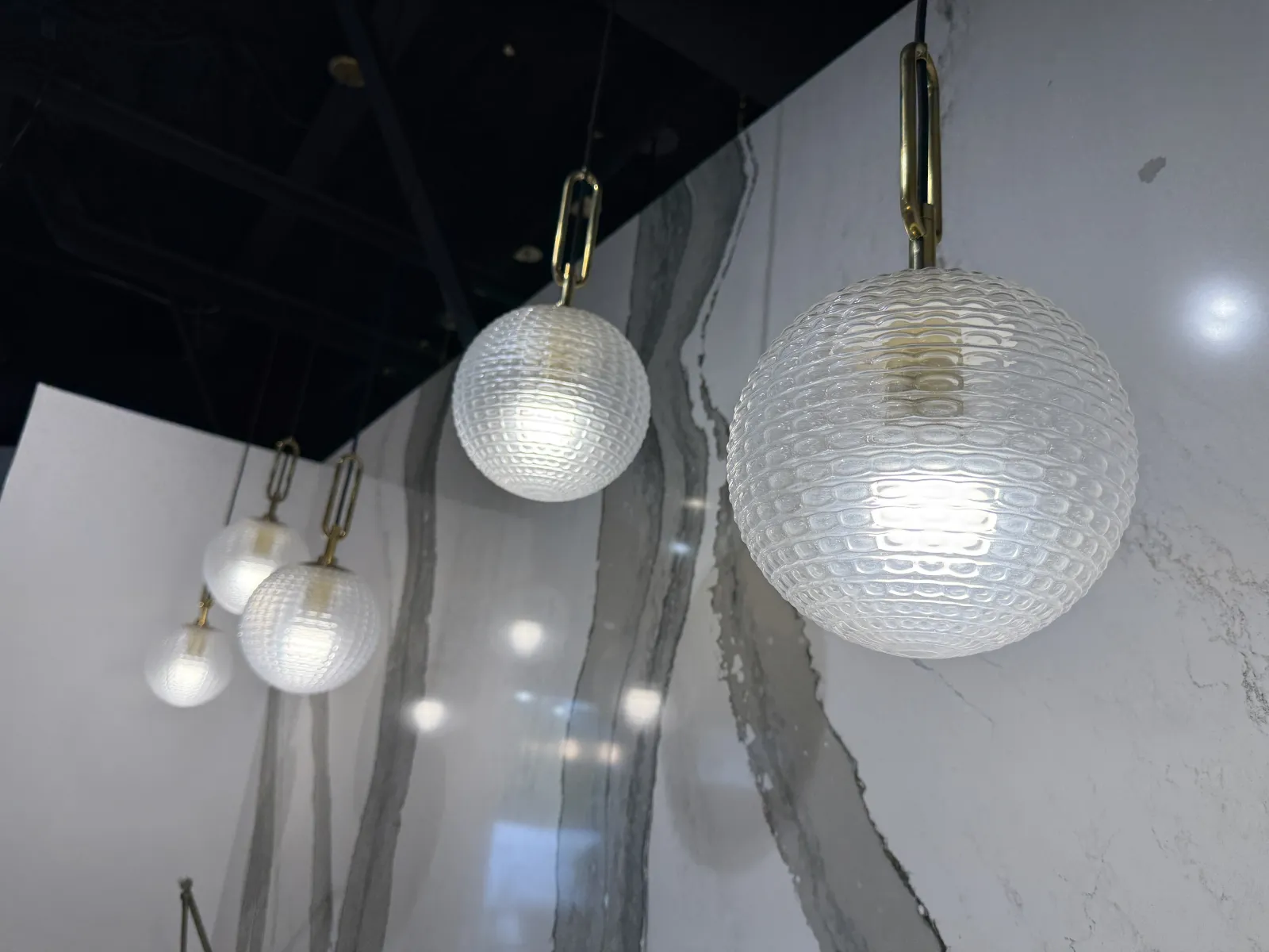 Cluster of five textured glass globe pendant lights hanging against a marble wall with black ceiling.