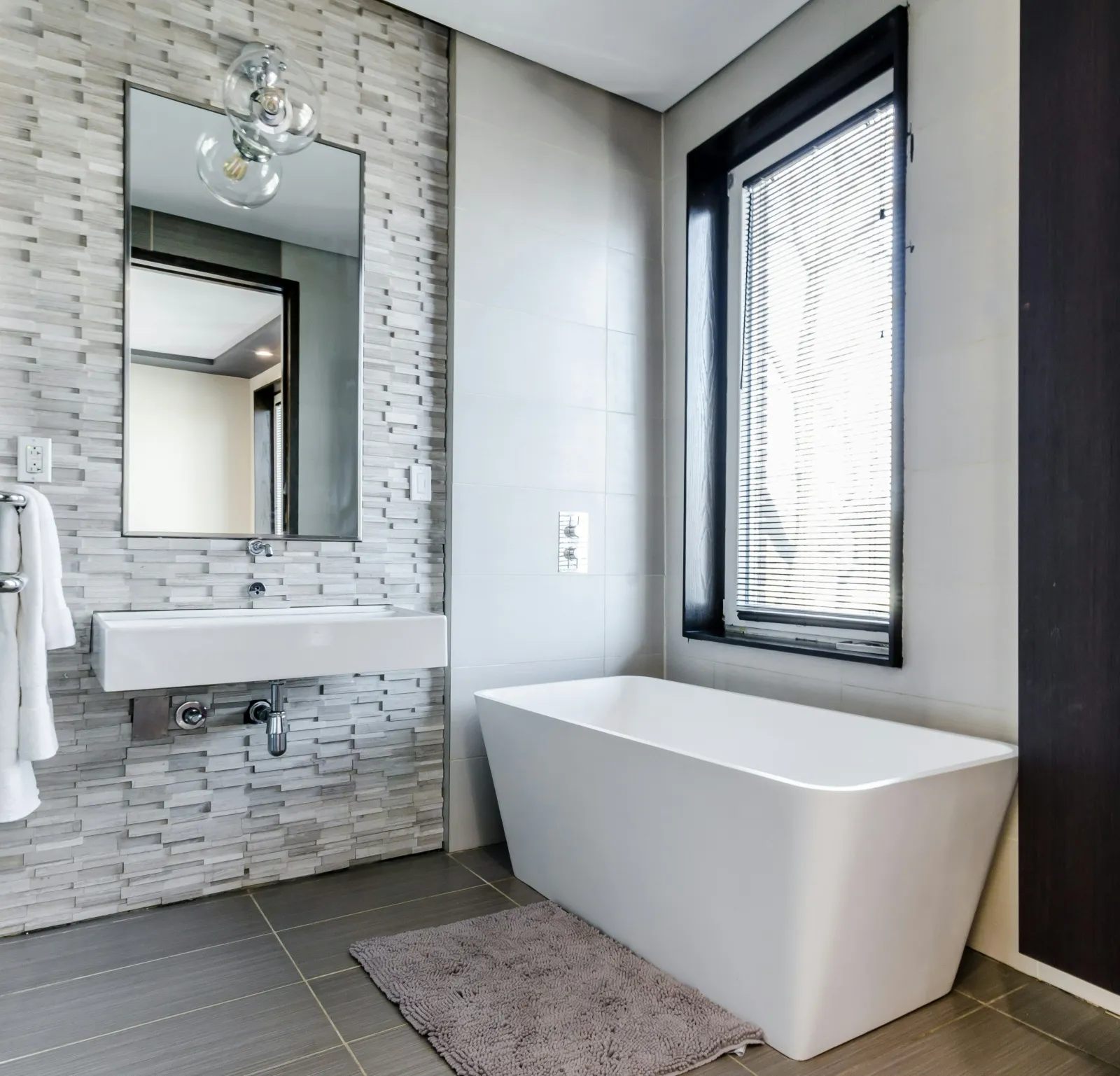 Modern bathroom featuring a freestanding tub, large mirror, and stylish tile accents.