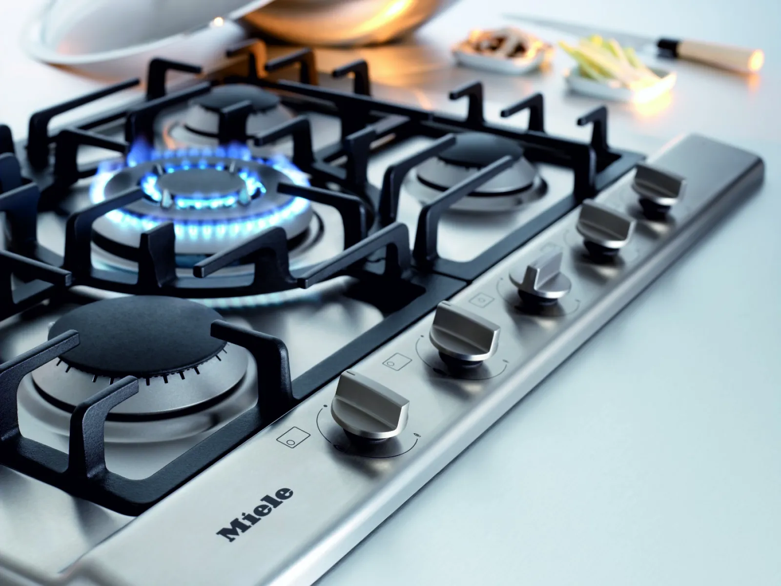 Close-up of a sleek Miele gas cooktop with illuminated burner and modern controls.