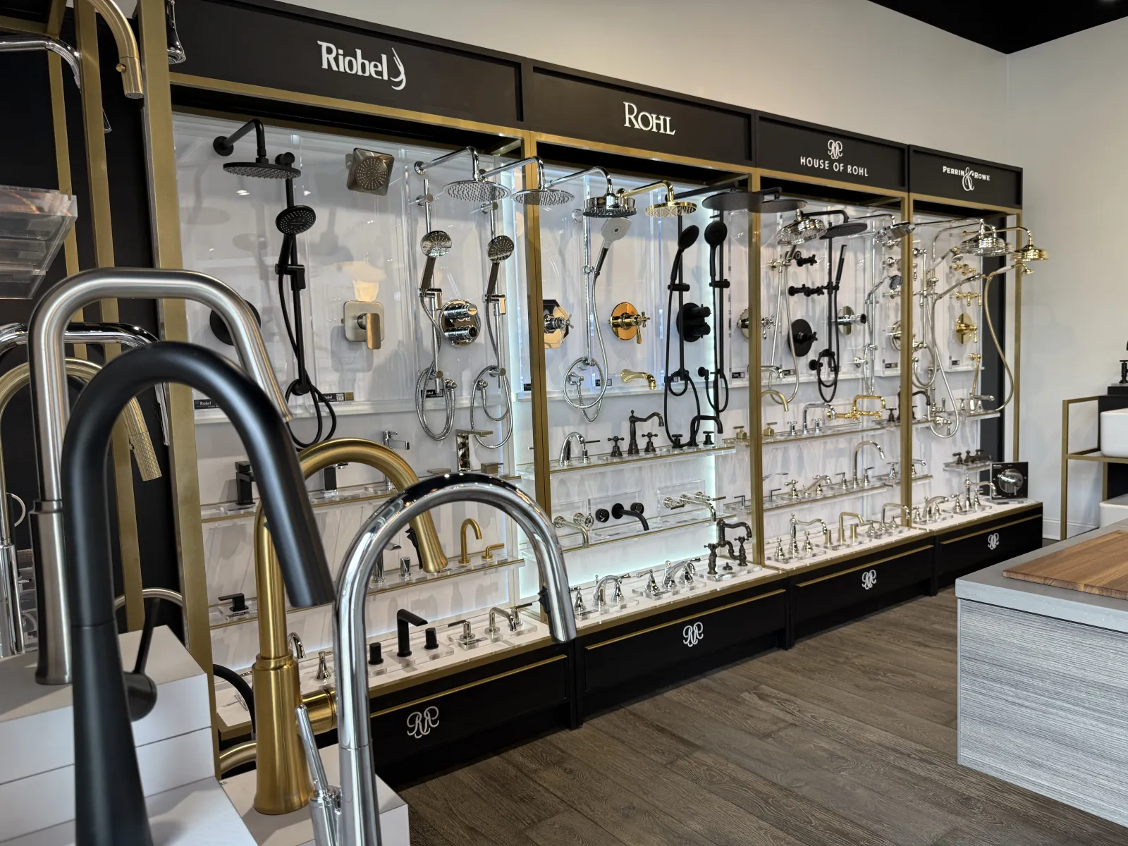 Showroom display of various luxury kitchen and bathroom faucets and showerheads in chrome, black, and gold finishes.
