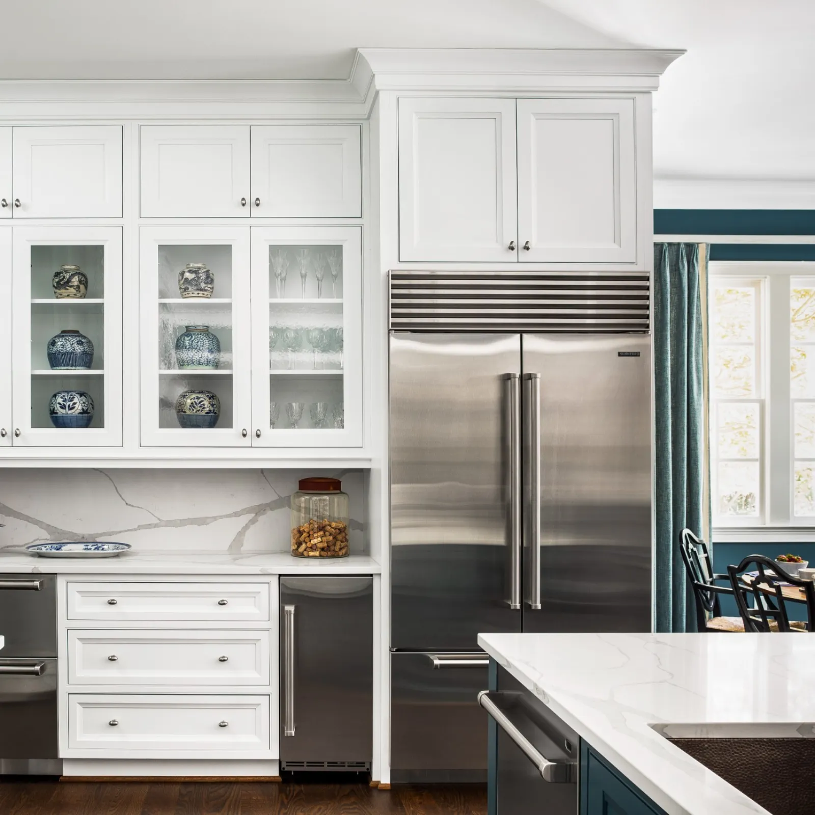 Modern kitchen with white cabinetry, stainless steel refrigerator, glass-front cabinets, and marble countertops.