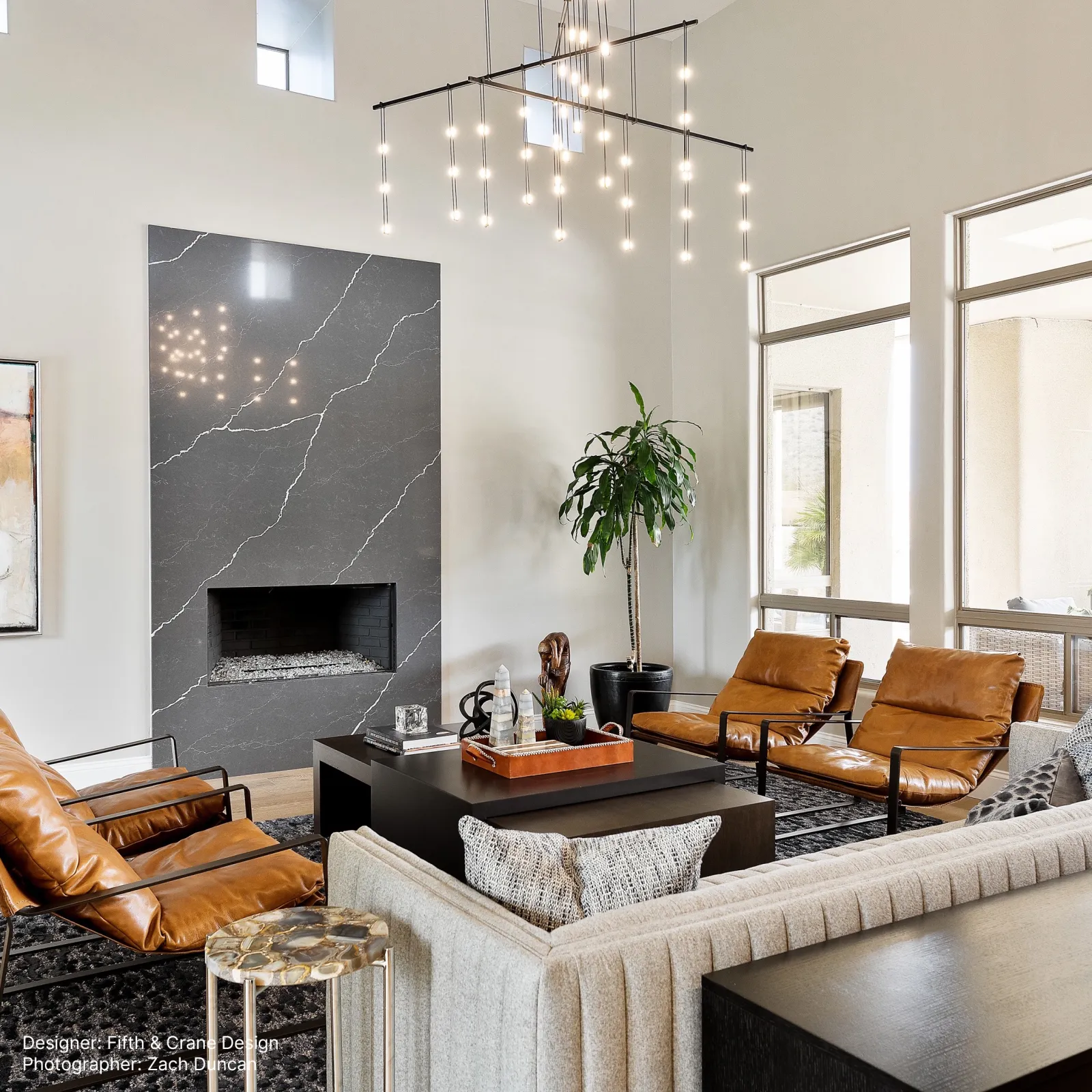 Modern living room with leather chairs, gray sofa, black coffee table, large plant, and minimalist fireplace design.