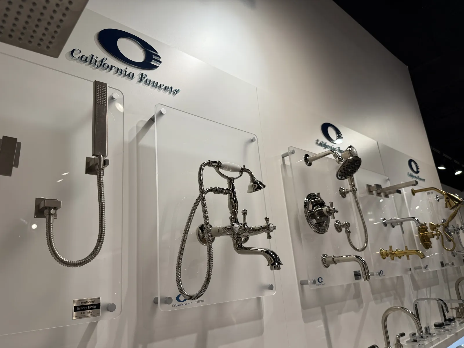 Display of various stylish chrome and brass bathroom faucets and showerheads mounted on a wall in a showroom.
