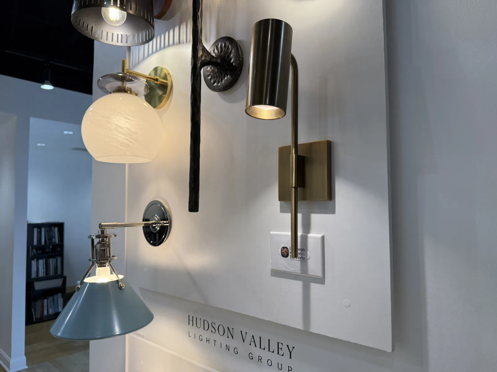 Various modern wall-mounted light fixtures displayed on a white panel with a Hudson Valley Lighting Group sign