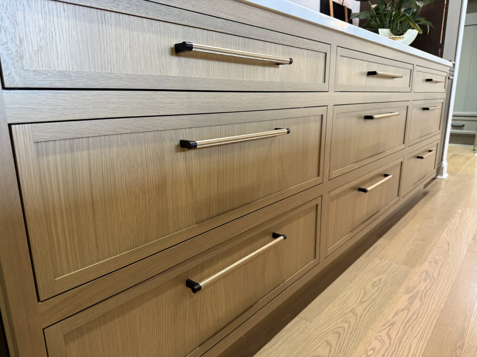 Close-up of modern light wood kitchen cabinets with sleek horizontal metal handles and hardwood floor.