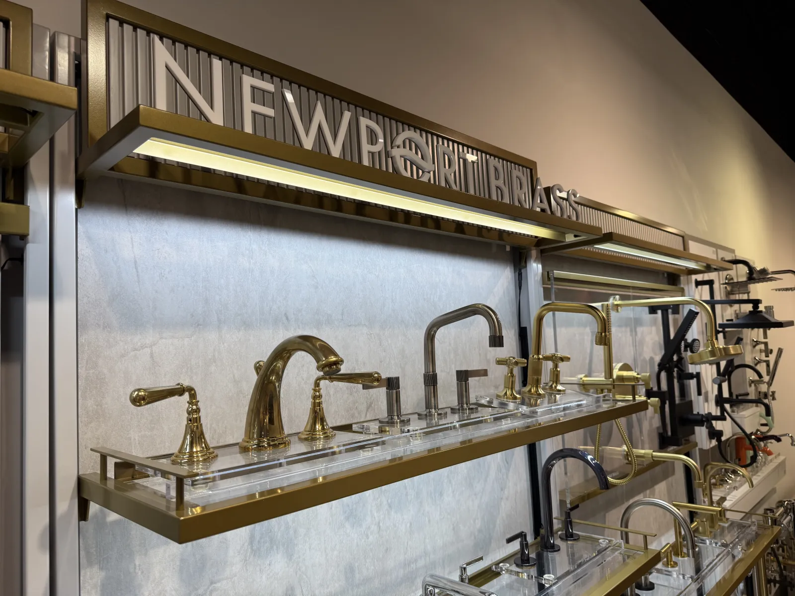 Display of various brass and matte black kitchen and bathroom faucets on wall-mounted shelves.