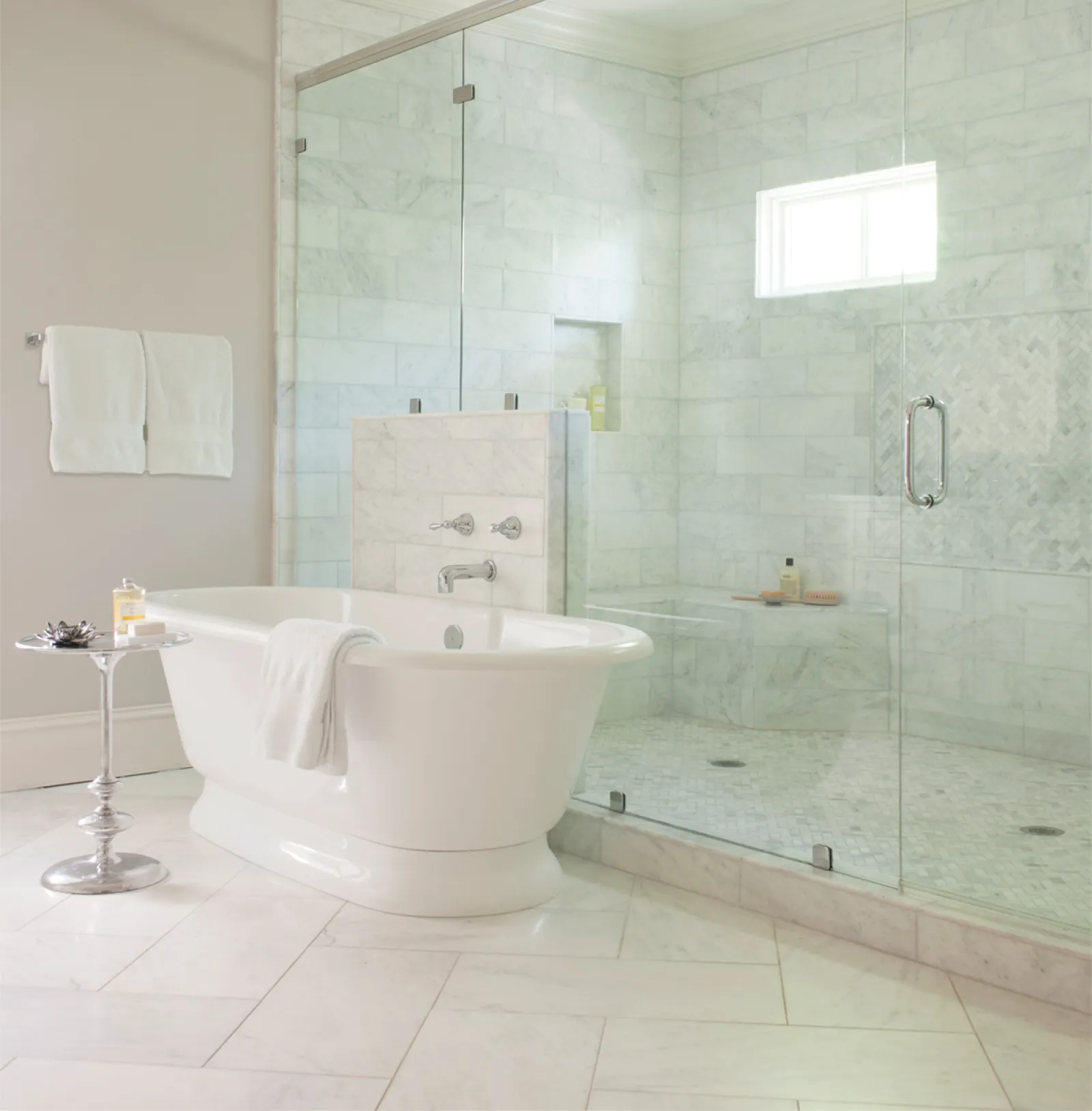 Modern bathroom with white freestanding tub, glass shower enclosure, marble tiles, and chrome fixtures