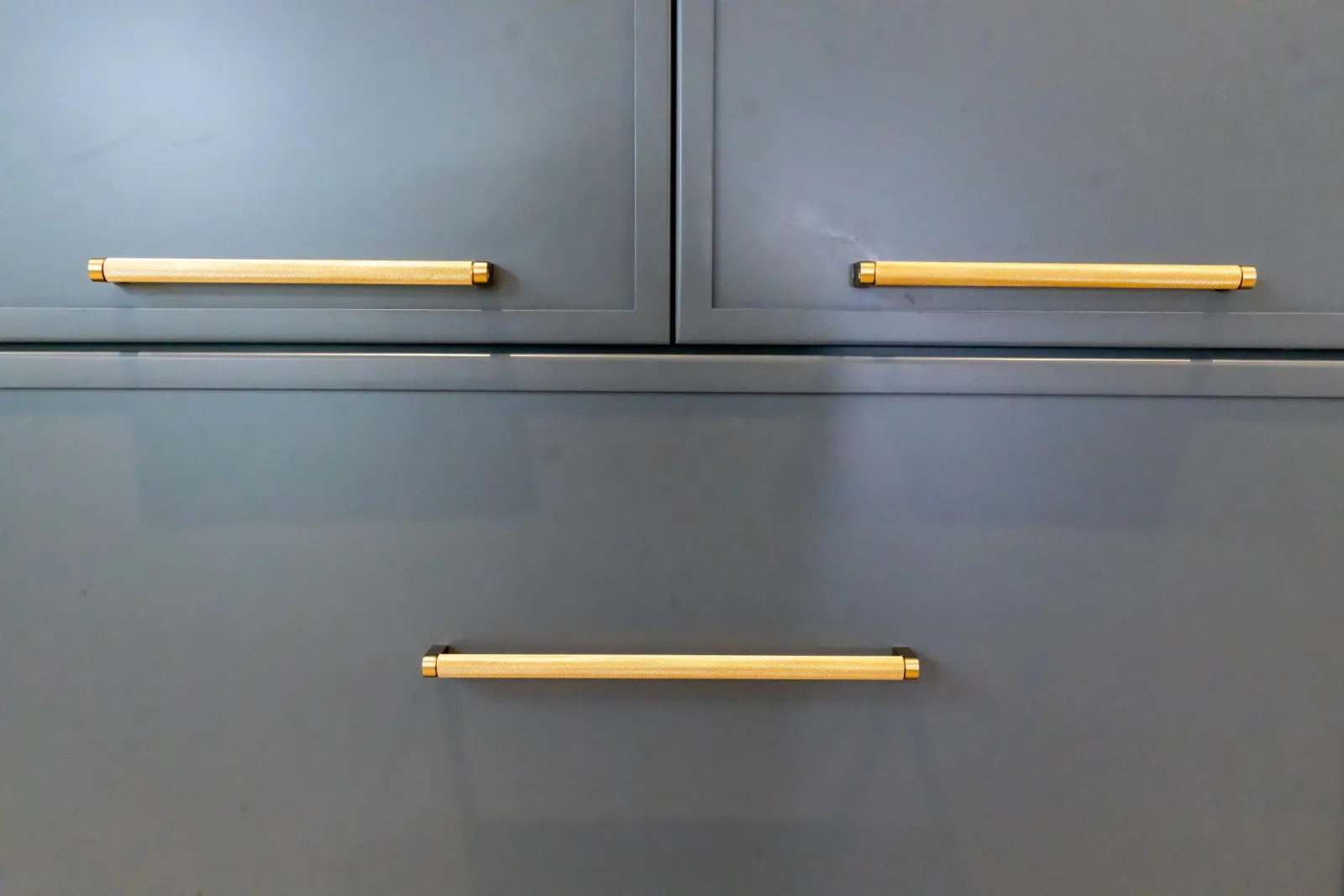 Close-up of modern gray cabinet drawers with brass handles.