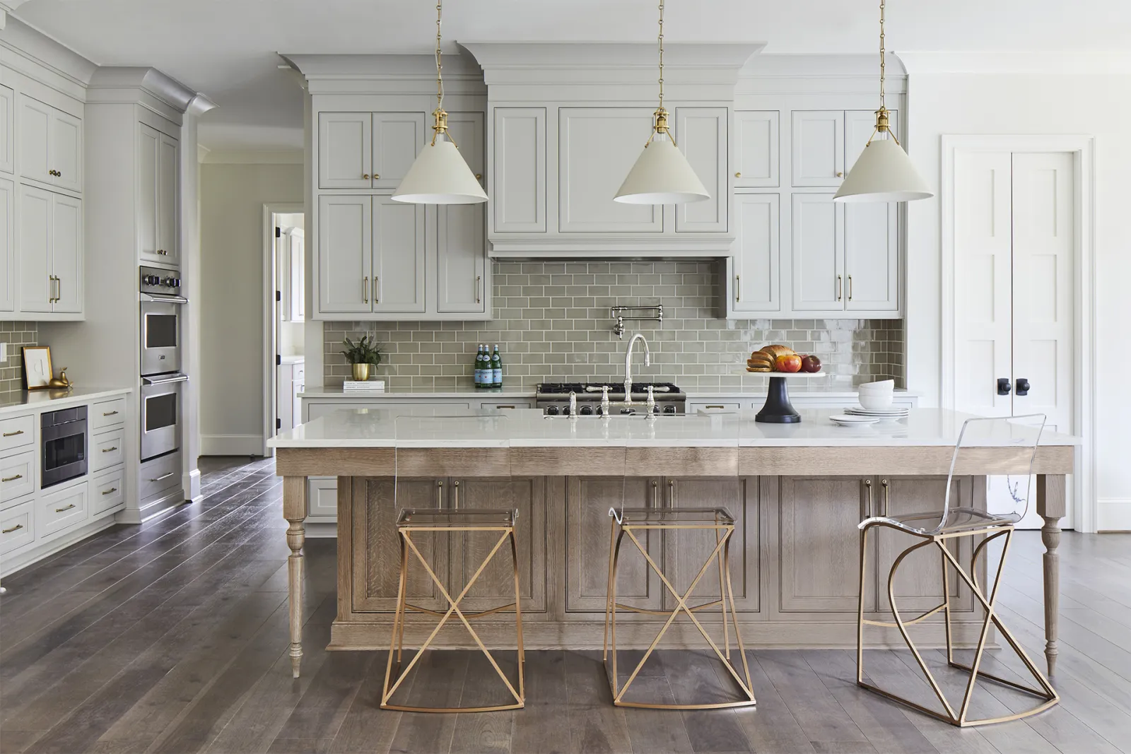 Bright modern kitchen with white cabinetry, large island with wooden base, and three unique metal stools.