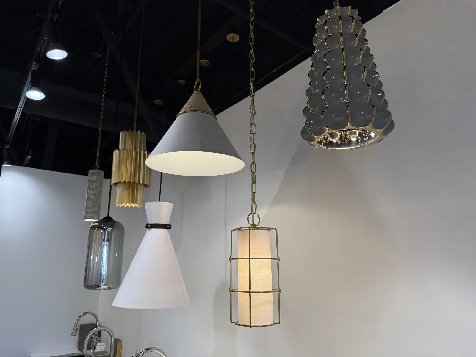 Stylish modern pendant lamps with varied shapes and materials hanging against a white wall and black ceiling.