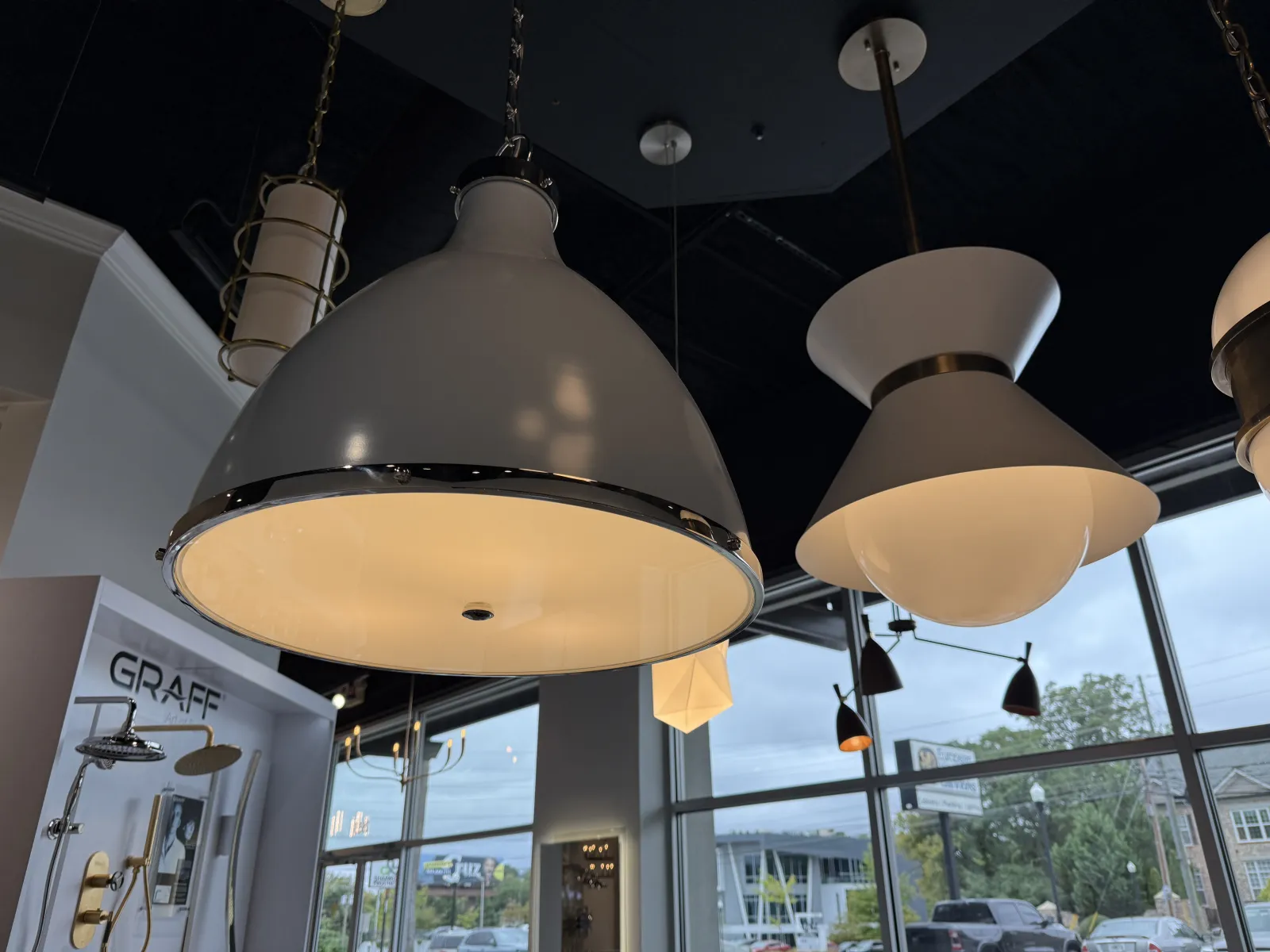 Modern pendant lights hanging from a dark ceiling in a showroom with large windows and outdoor view