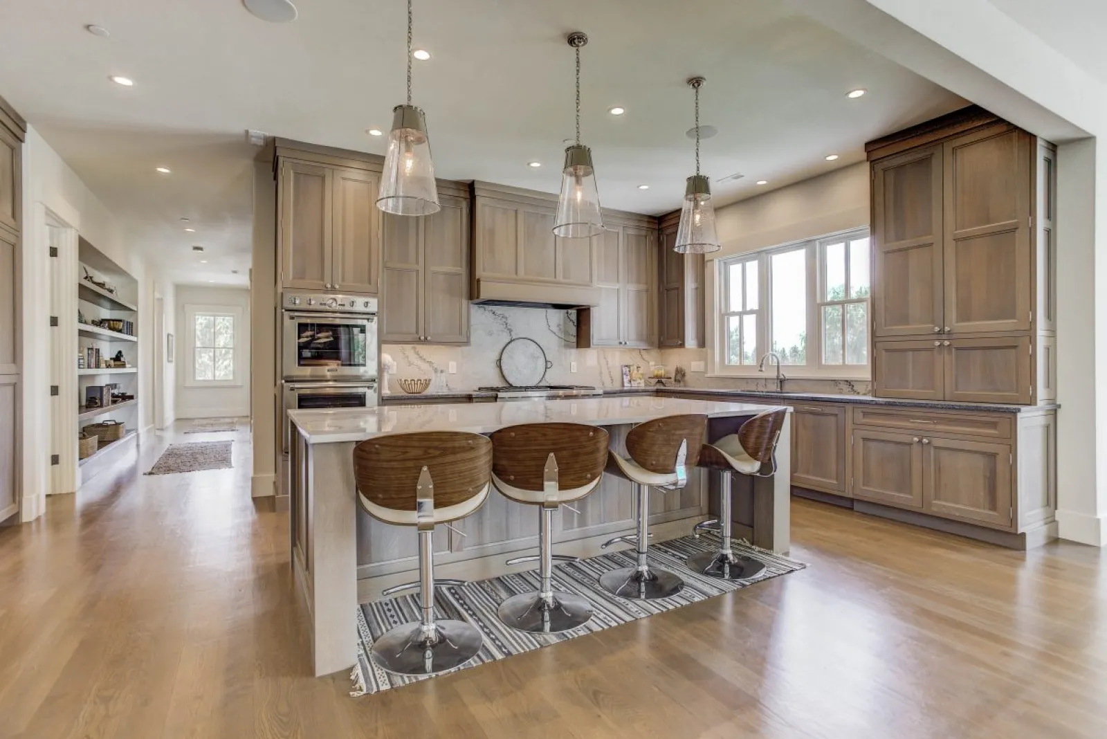 Modern kitchen with wood cabinetry, marble countertops, four bar stools, pendant lights, and hardwood floors