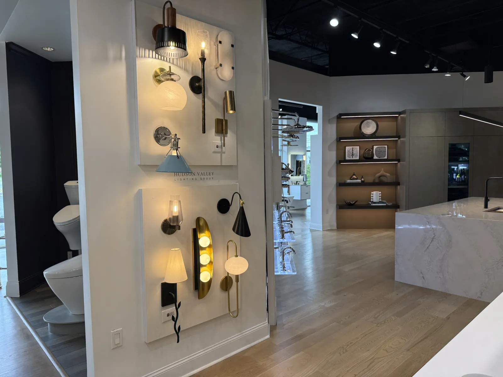Modern lighting fixtures displayed on wall panels in a stylish showroom with wooden floors and kitchen island.