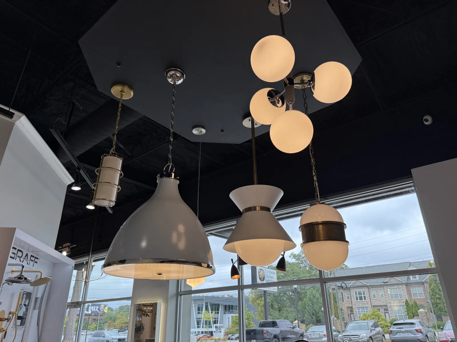 Modern pendant lights and globe chandeliers hanging from a black ceiling in a showroom with large windows.