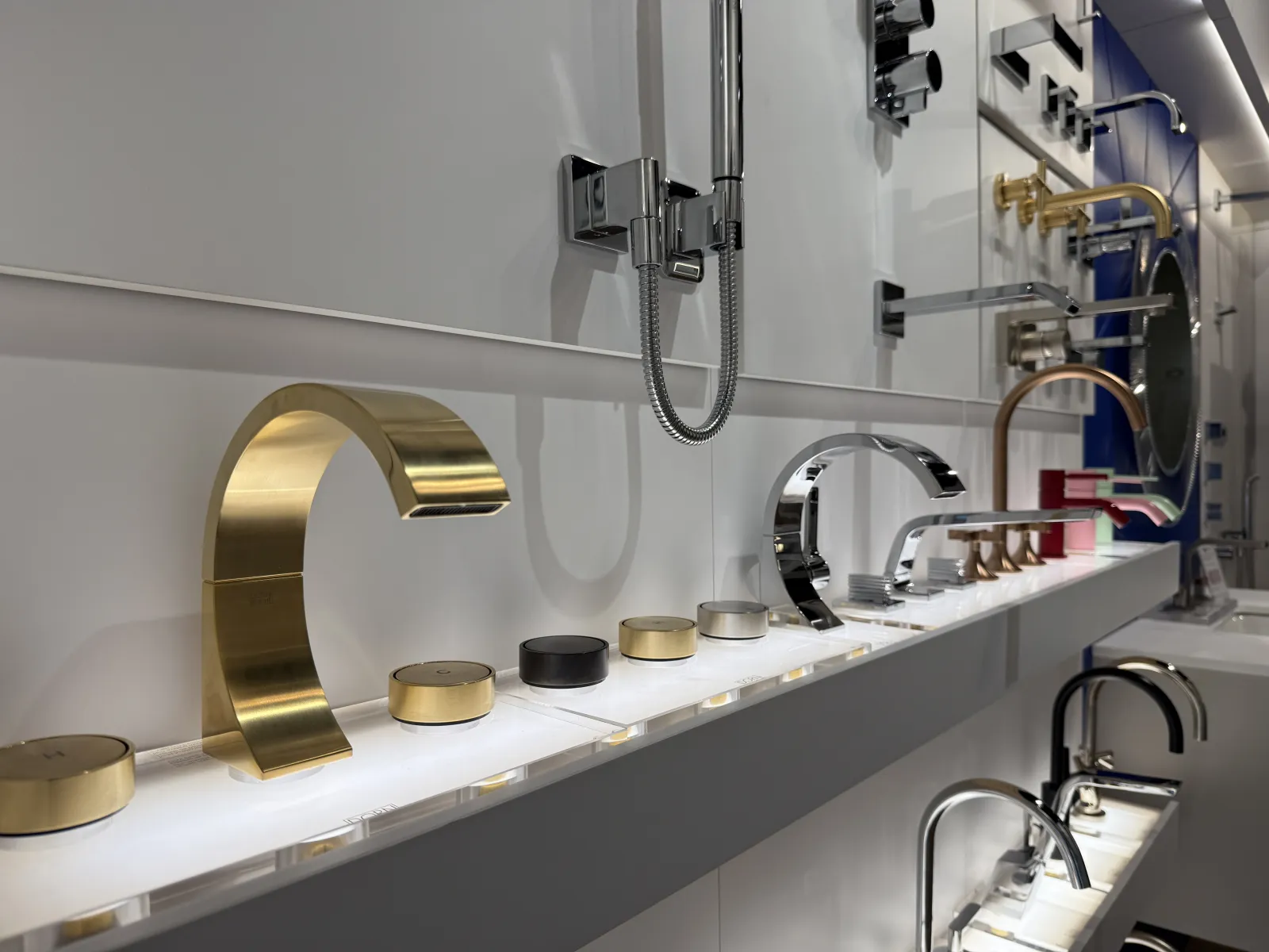 Display of modern bathroom faucets and controls in metallic finishes including gold, chrome, and black on shelves.