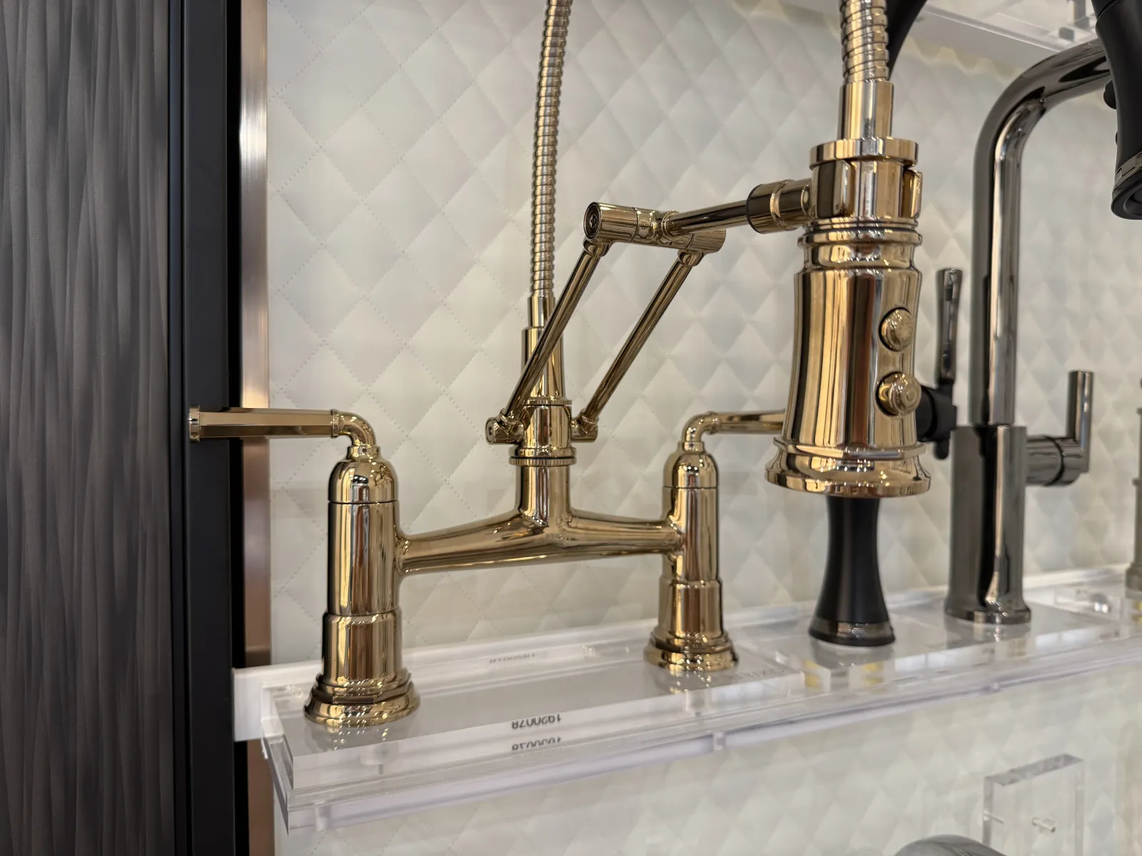 Polished gold-tone kitchen faucet with dual handles and flexible spout against textured white background.