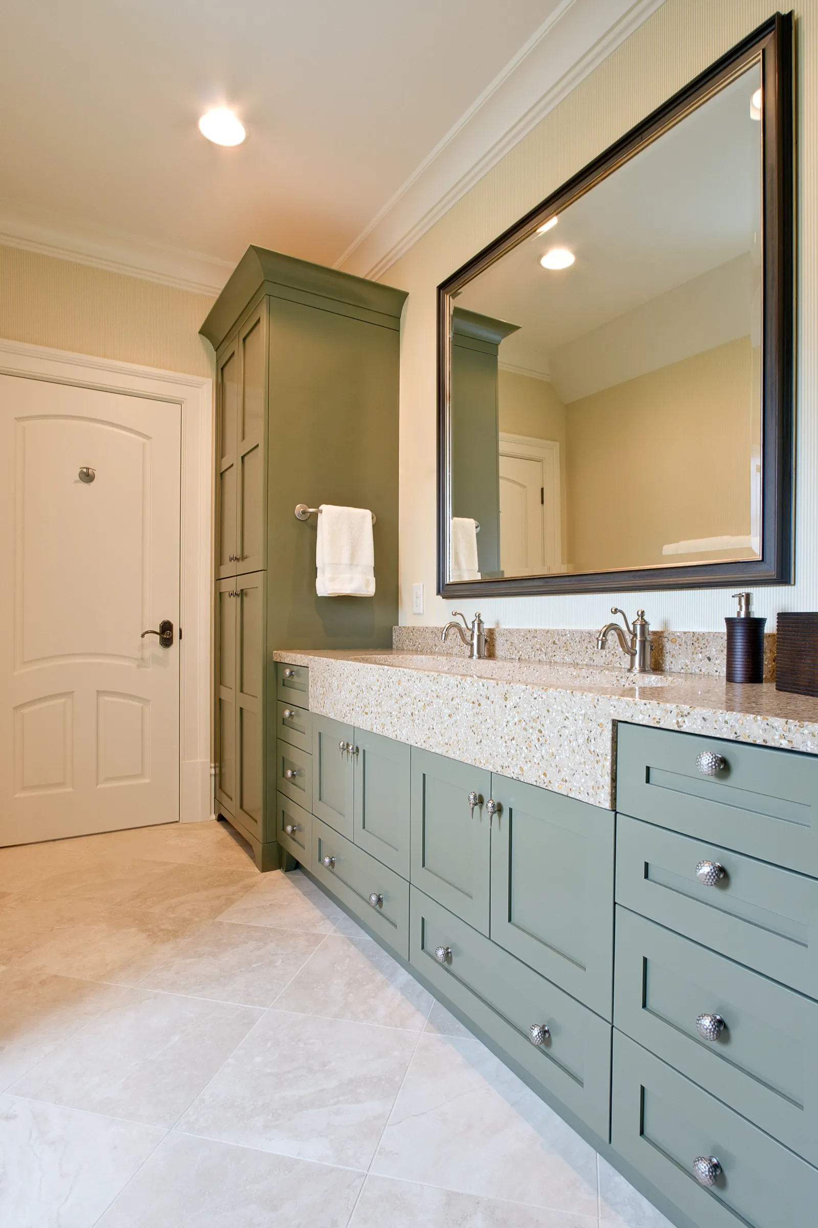 Modern bathroom with green cabinetry, large mirror, dual sinks, beige quartz countertop, and tiled floor.