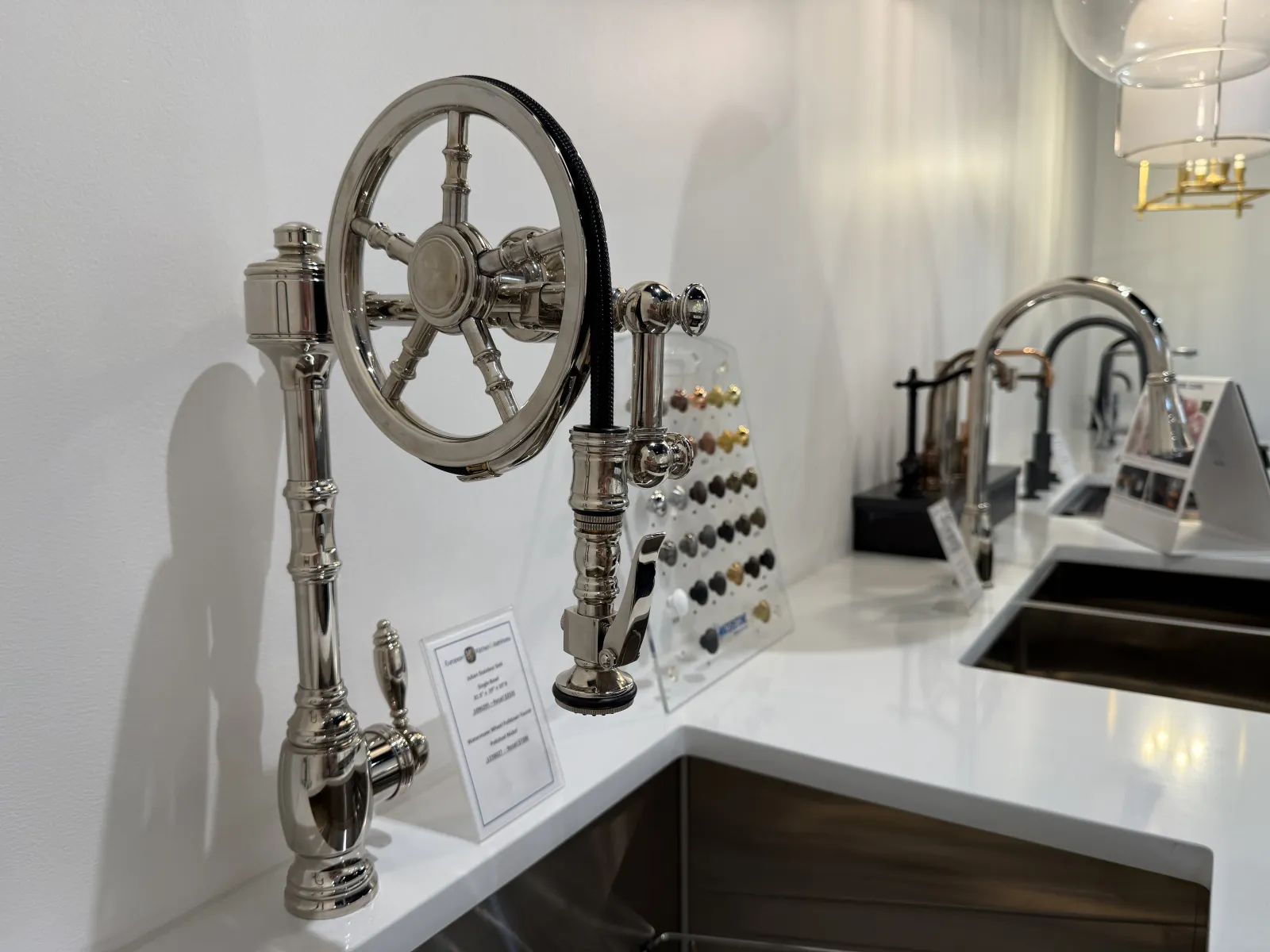 Modern kitchen faucet with a polished metal steering wheel design and white countertop with sink.
