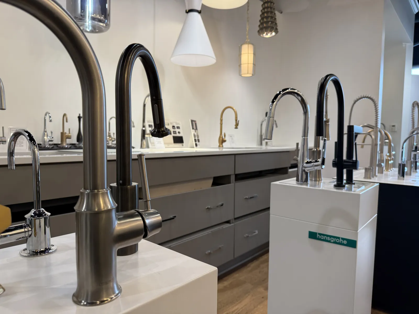 Modern kitchen faucets displayed in a showroom with various designs on countertops and pendant lights above