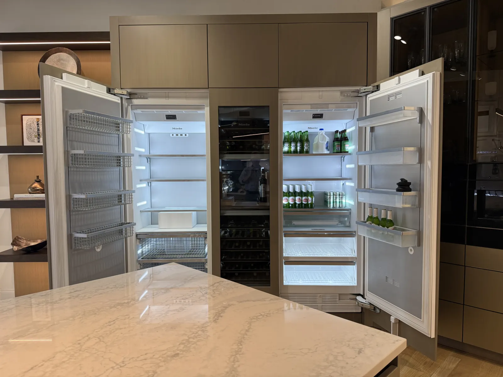 Modern kitchen with double open refrigerators and a wine cooler in the center, featuring integrated cabinetry design.