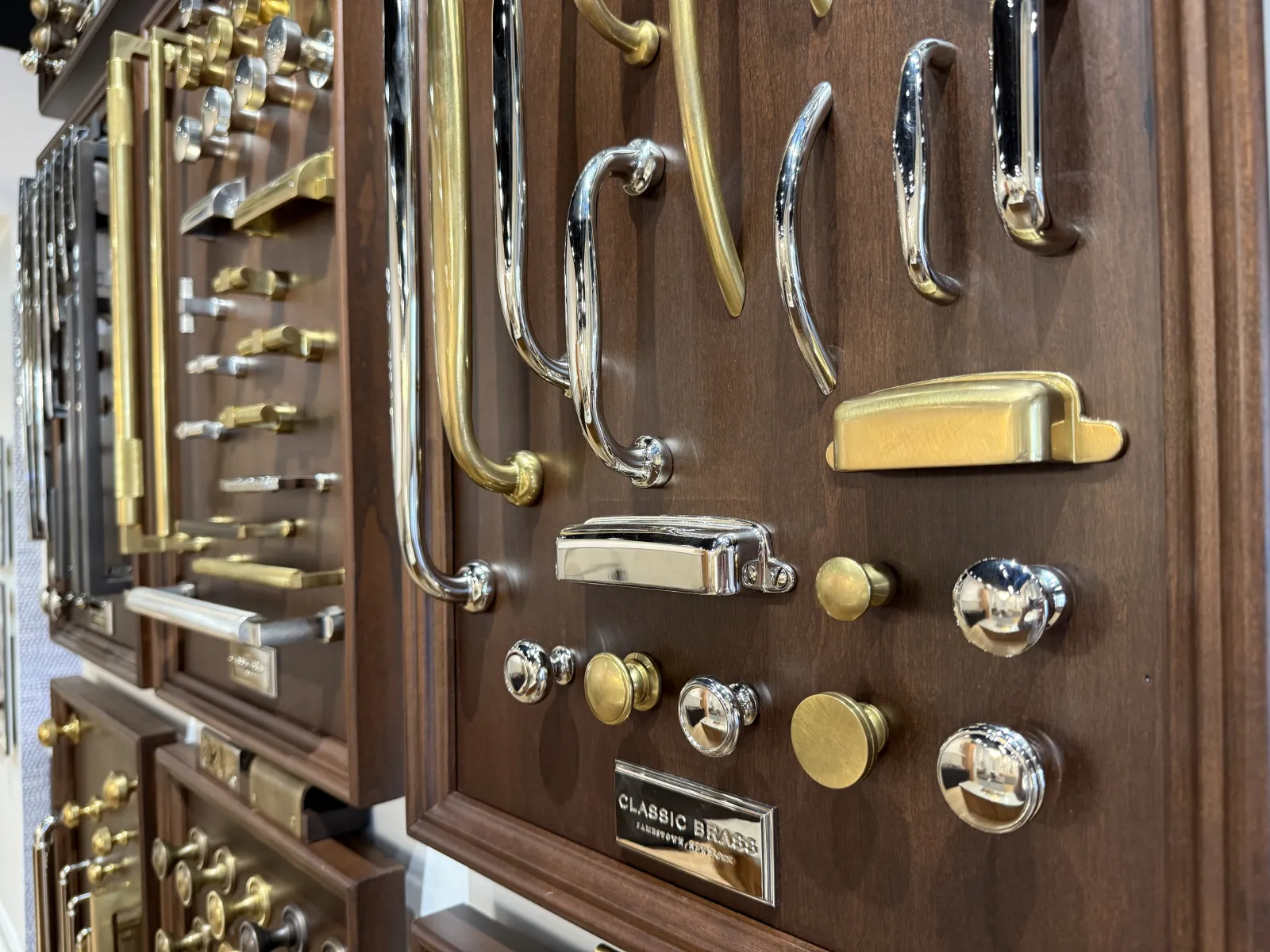 Various brass and chrome cabinet handles and knobs displayed on wooden boards in a showroom.
