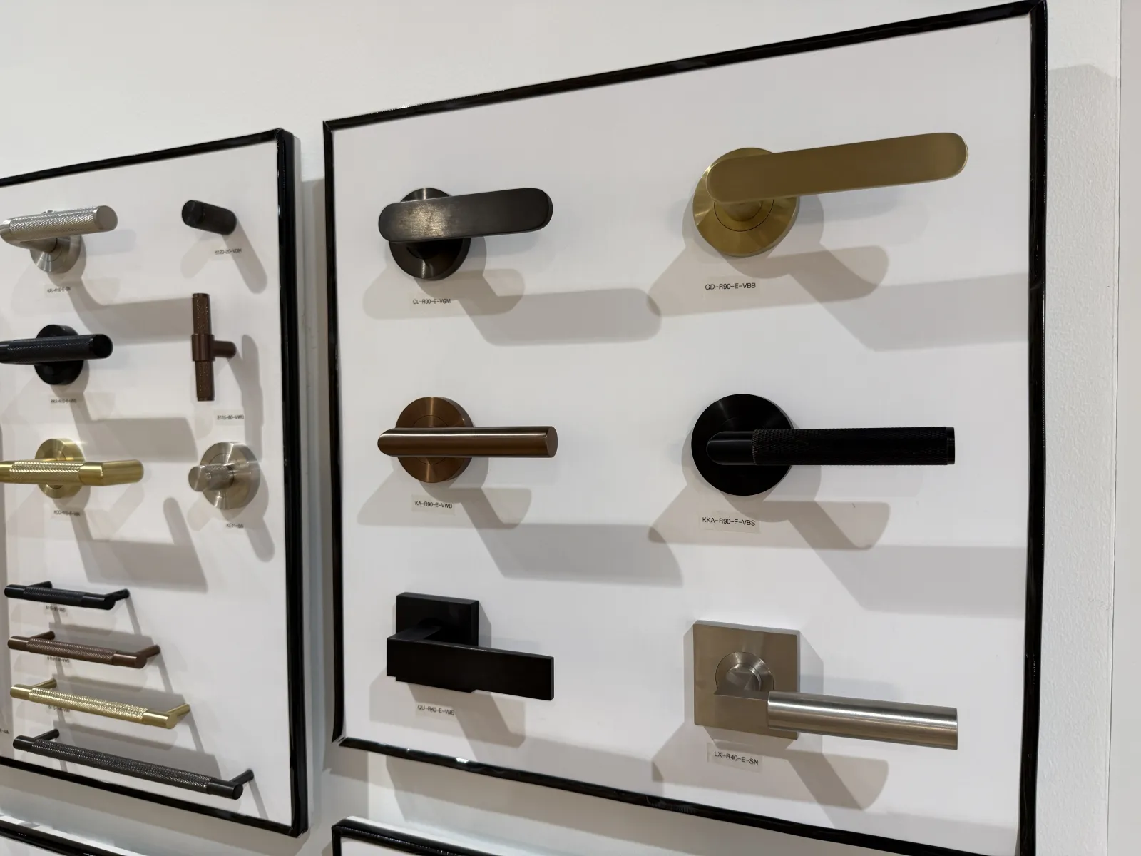 Display of various modern door handles in different finishes mounted on white boards against a wall.