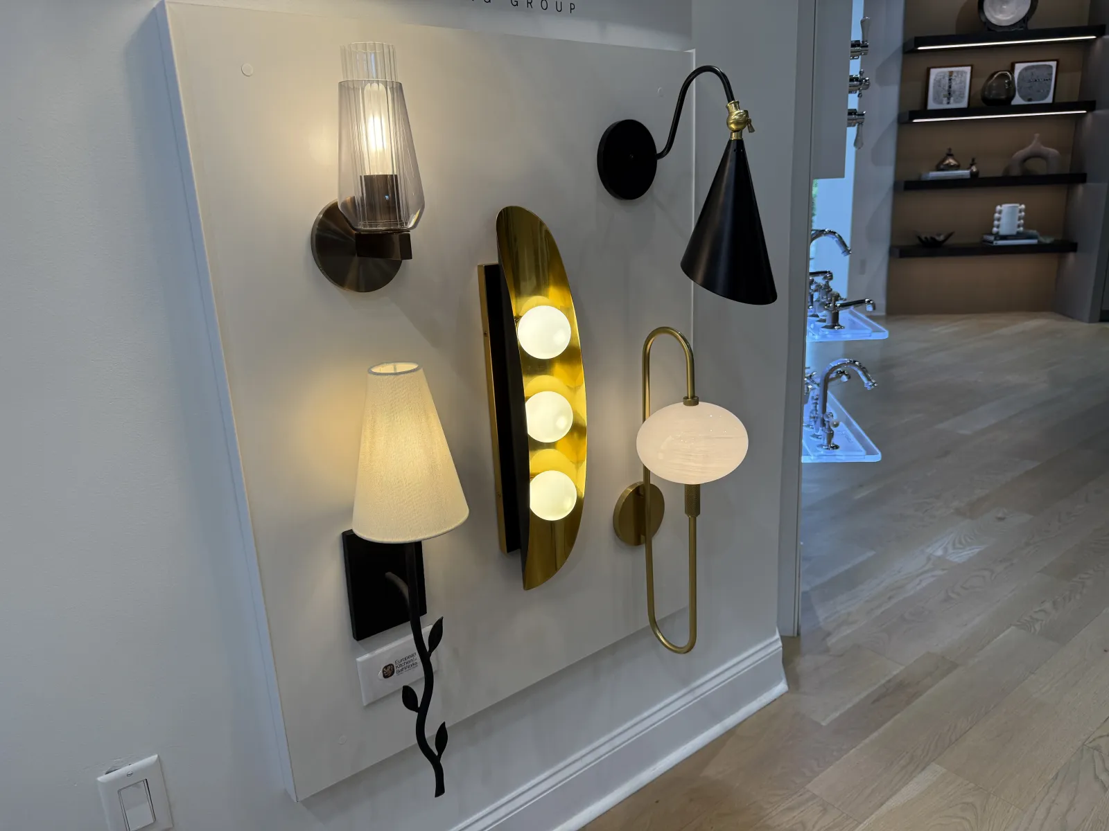 Modern wall lamps with varied designs and lighting styles displayed on a white panel in a showroom.