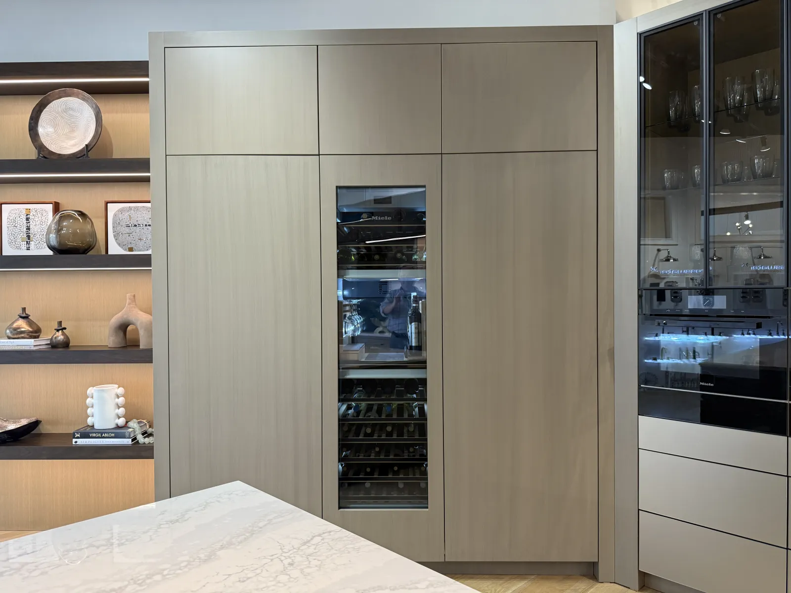 Modern kitchen with built-in wood cabinetry, glass-front wine cooler, and marble countertop island.