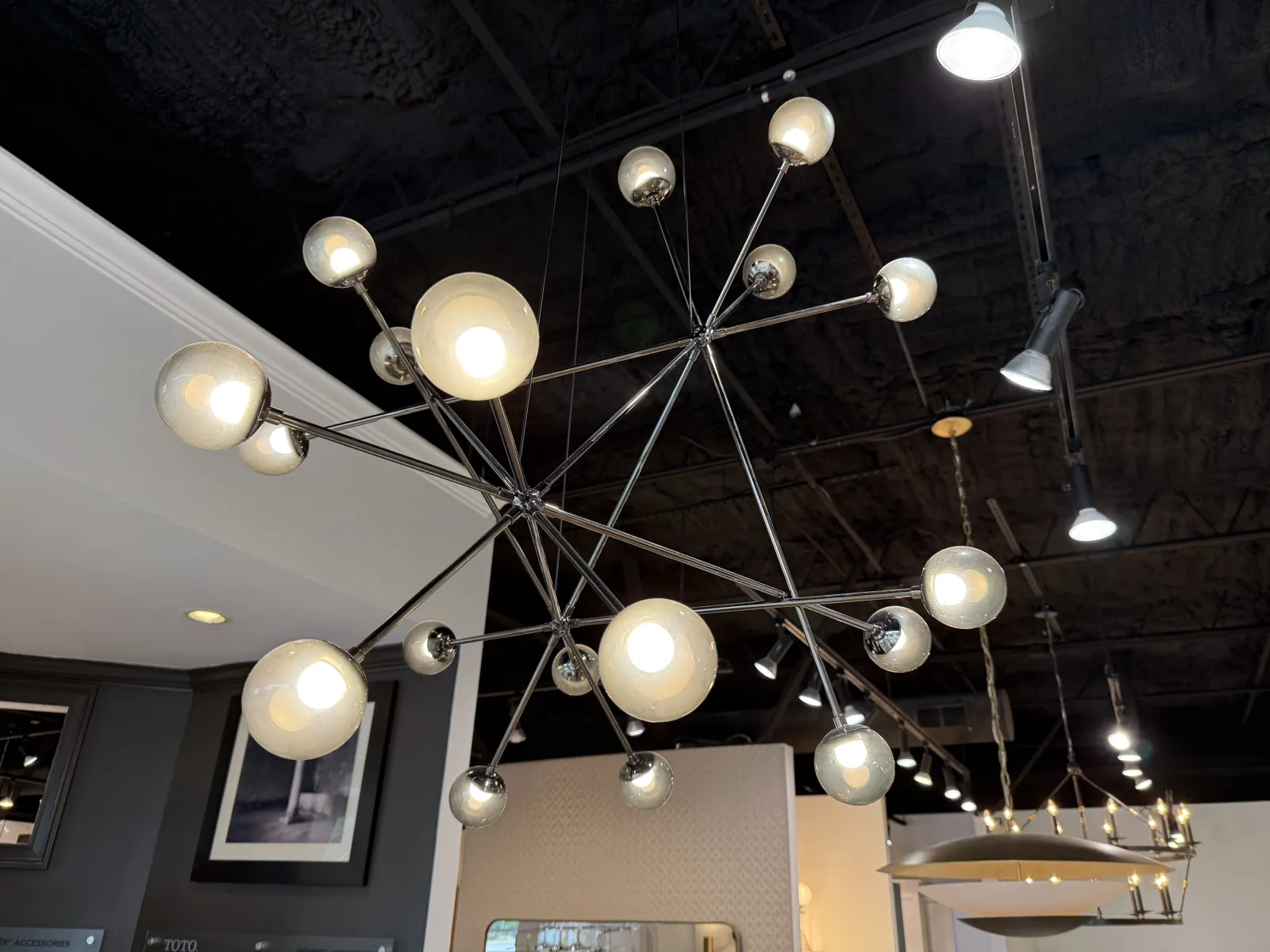 Modern chandelier with multiple glowing spherical bulbs hanging from a black ceiling in a contemporary room.