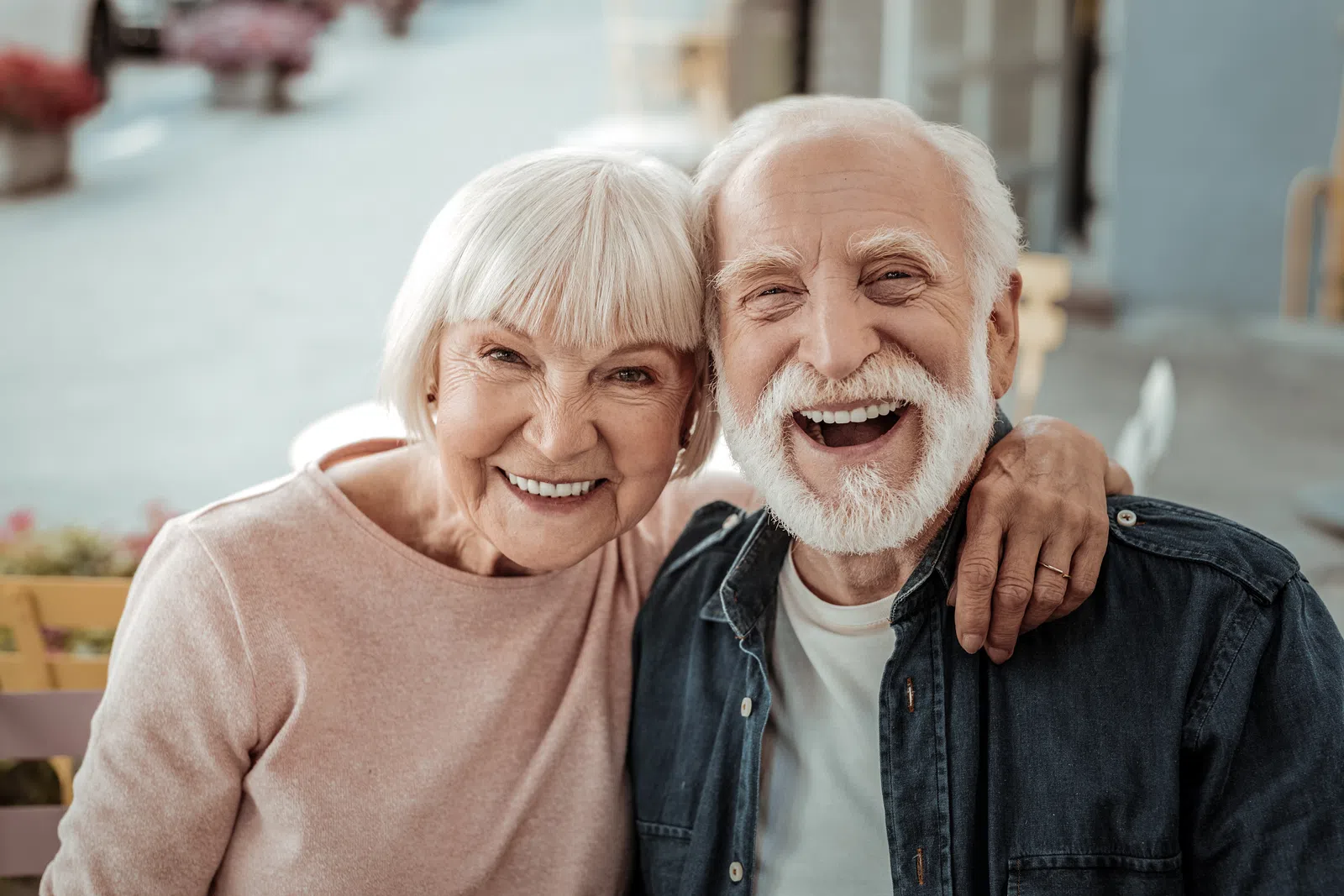 Happy elderly couple smiling outdoors with arm around each other, showing warmth and companionship.