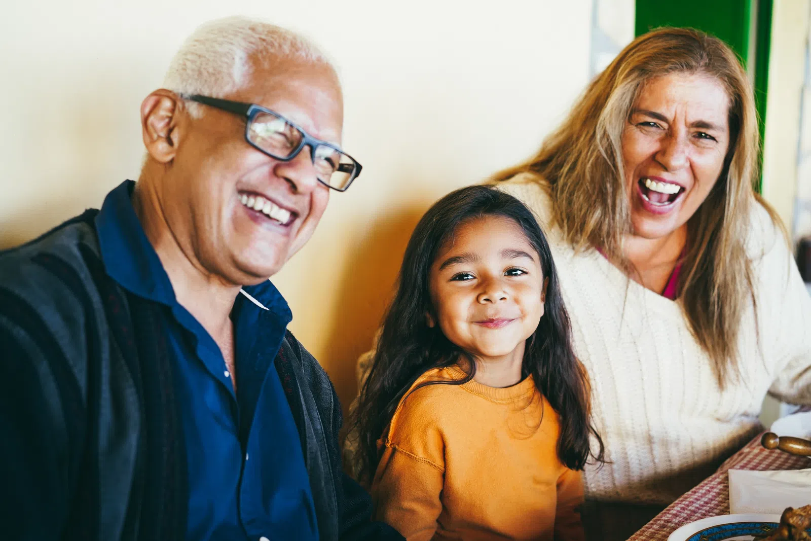 Joyful multigenerational family laughing together at a meal indoors with warm natural light and cozy atmosphere