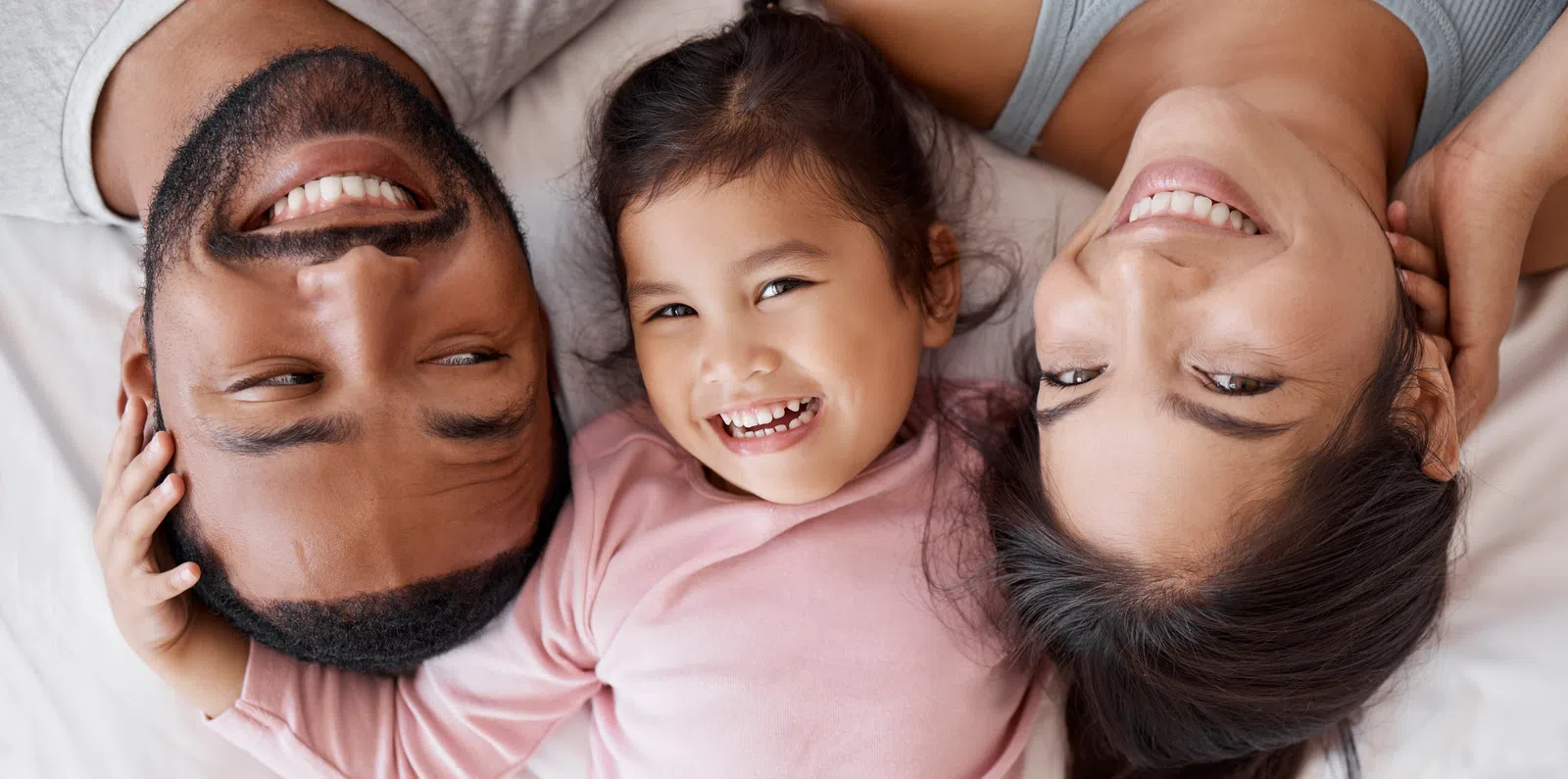 Happy family of three lying down together smiling, showing close bond and joyful moments