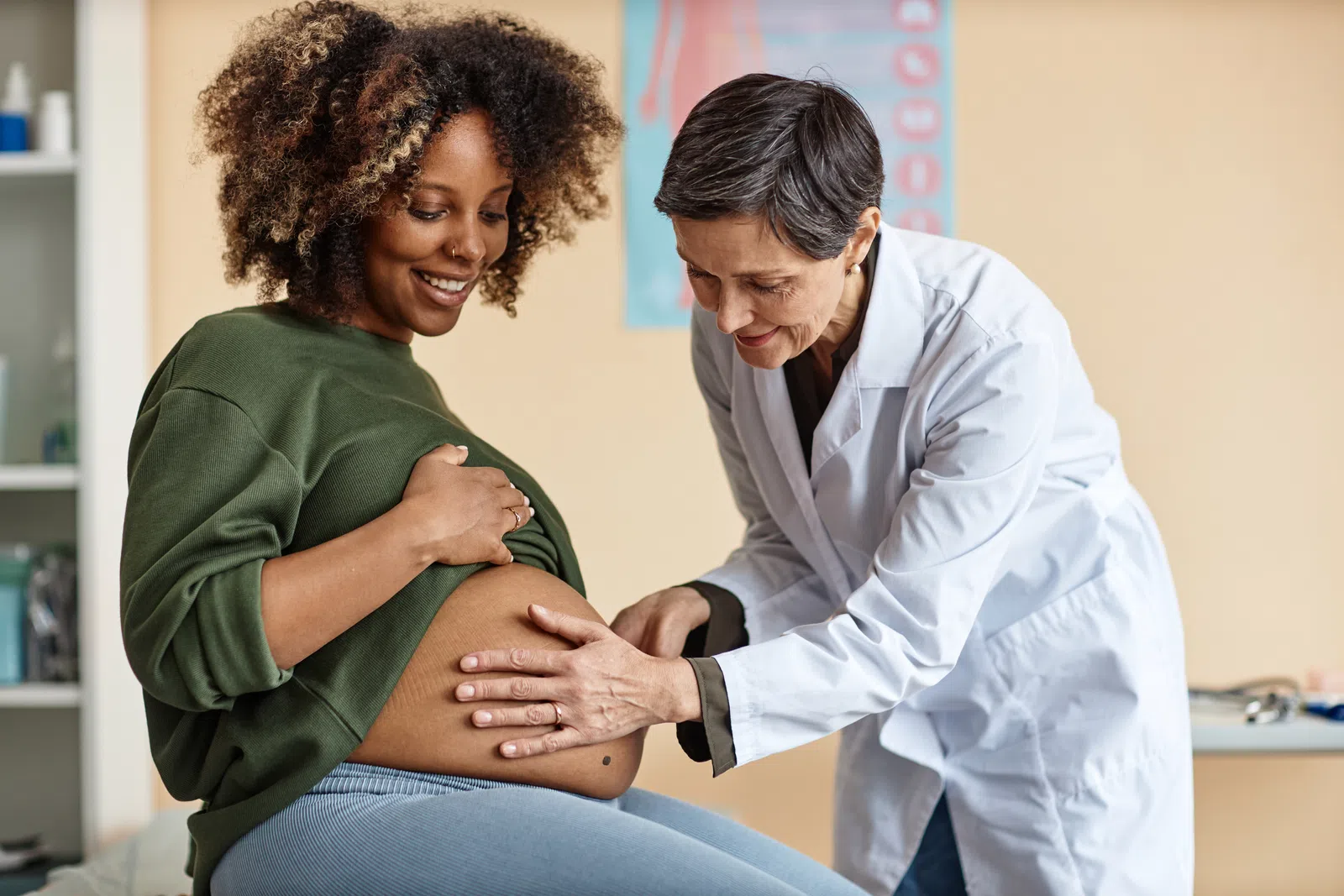 Pregnant woman smiling as doctor examines her baby bump in a medical office during prenatal checkup.